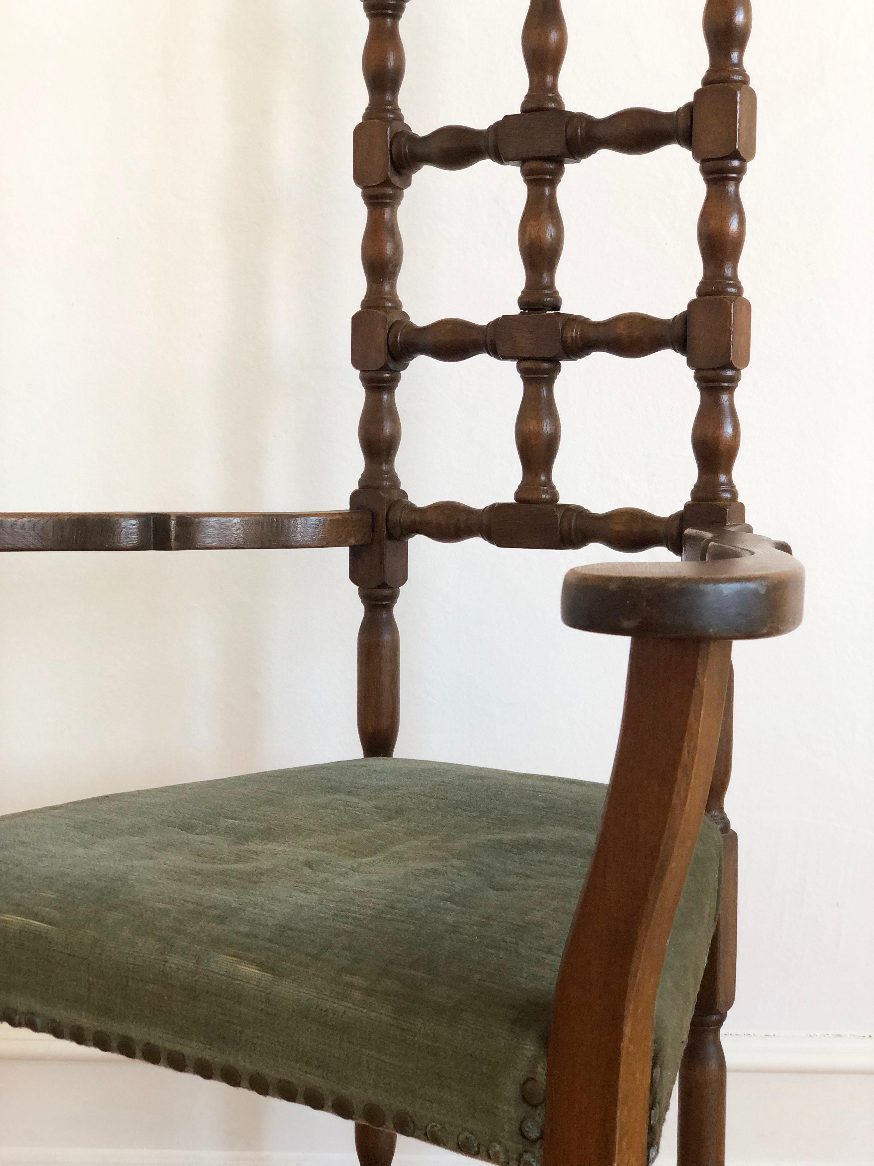Bellamente fabricado hacia 1800-1850, este sillón español de madera maciza presenta un clásico respaldo alto con seis husillos torneados y reposabrazos rectos. El asiento casi triangular está retapizado en tela verde con clavos decorativos de latón.