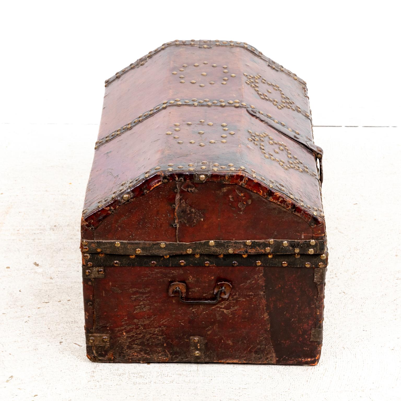 Circa 18th century Spanish leather trunk with two side handles decorated throughout with metal nail head trim and constructed with metal hardware. The piece features metal nail head designs including octagonal patterns on the lid and round oval