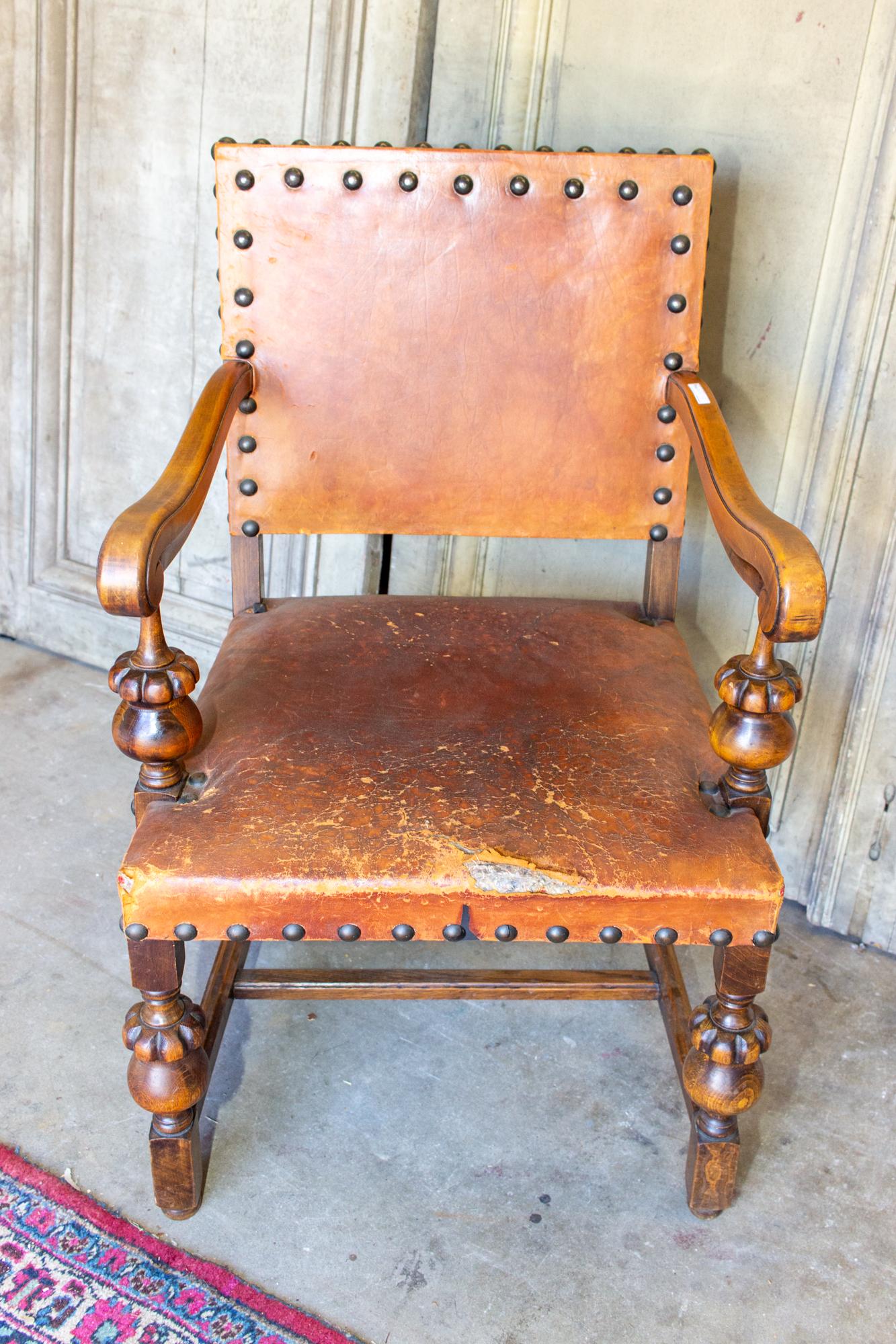 This is an antique Spanish wood & leather armchair with beautiful carvings in the frame and patinated brass nailhead details. The leather is a rich deep cognac color and does have wear, patination and there is a tear on the front edge of the seat.