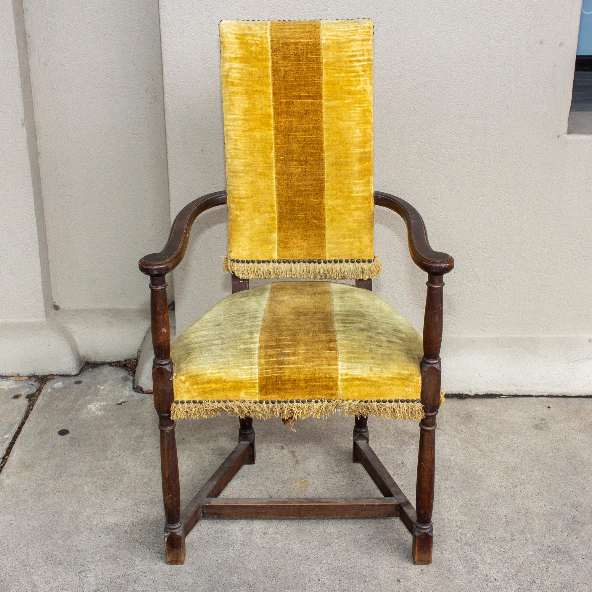 This antique Spanish chair is crafted with an oak frame and upholstered in a yellow velvet striped fabric with fringe detail and brass nail-head accents. The golden yellow stripe is wide with a deeper mustard shade at center and the coordinating