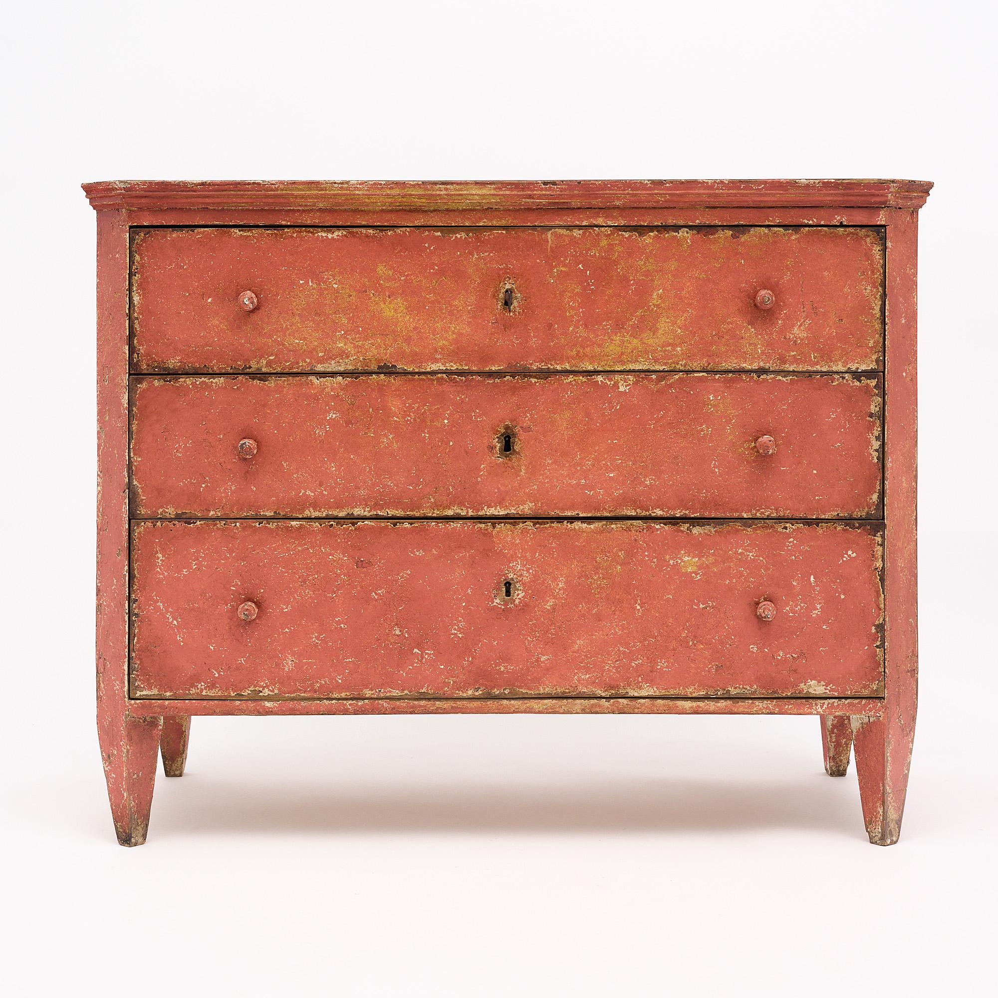 Chest from Spain featuring the original salmon colored paint and wonderful patina. The paint has wear consistent with age and shows a beautiful warm undertone beneath. The knobs are wood and match the chest. It is supported by tapered legs. The