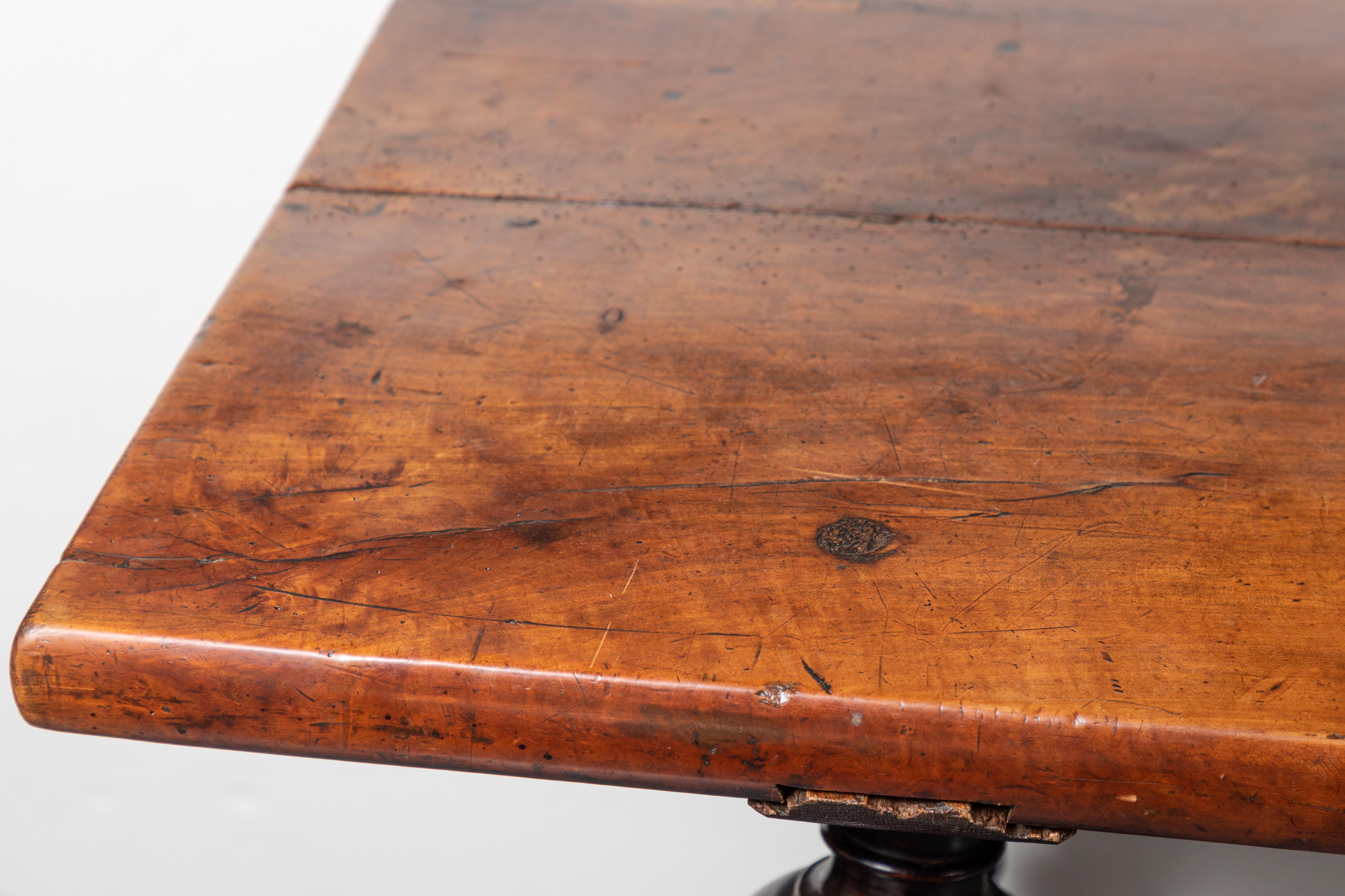Tisch aus feuerfestem Nussbaumholz mit handgeschmiedeter, schmiedeeiserner Bahre mit Schnörkeln. Die Platte aus zwei Brettern liegt über gestuften, gedrechselten Beinen.  Hergestellt aus antiken Elementen.