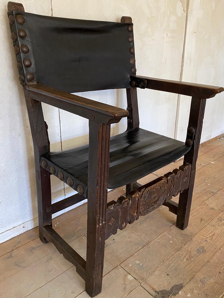 This Spanish walnut throne chair with a large wide seat made circa 1700. Made from well carved but simply done walnut the chair is centered on a leather covered seat and back with large antique nail heads. The stretcher in the front is chip carved