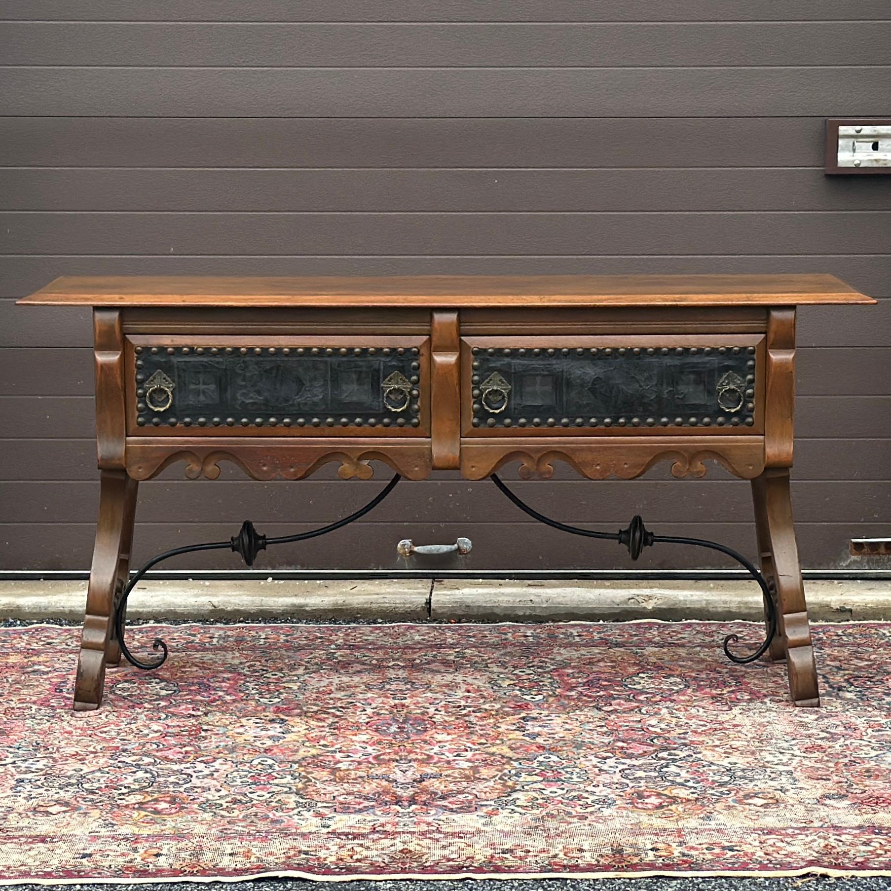 Crédence ancienne comprenant deux grands tiroirs avec façades en cuir estampé et grandes clous en laiton, quincaillerie en laiton massif, tablier sculpté, pieds en bois évasés avec fuseaux tournés, et brancards en fer forgé avec détails de perles en