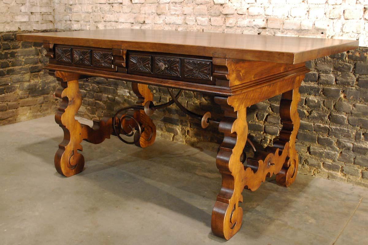 This beautiful Spanish baroque desk or writing table is made of solid walnut with lyre shaped legs joined by wrought iron stretchers. 
It has hand carved decoration across the front and back. The table features 6 drawers, three on each side, all