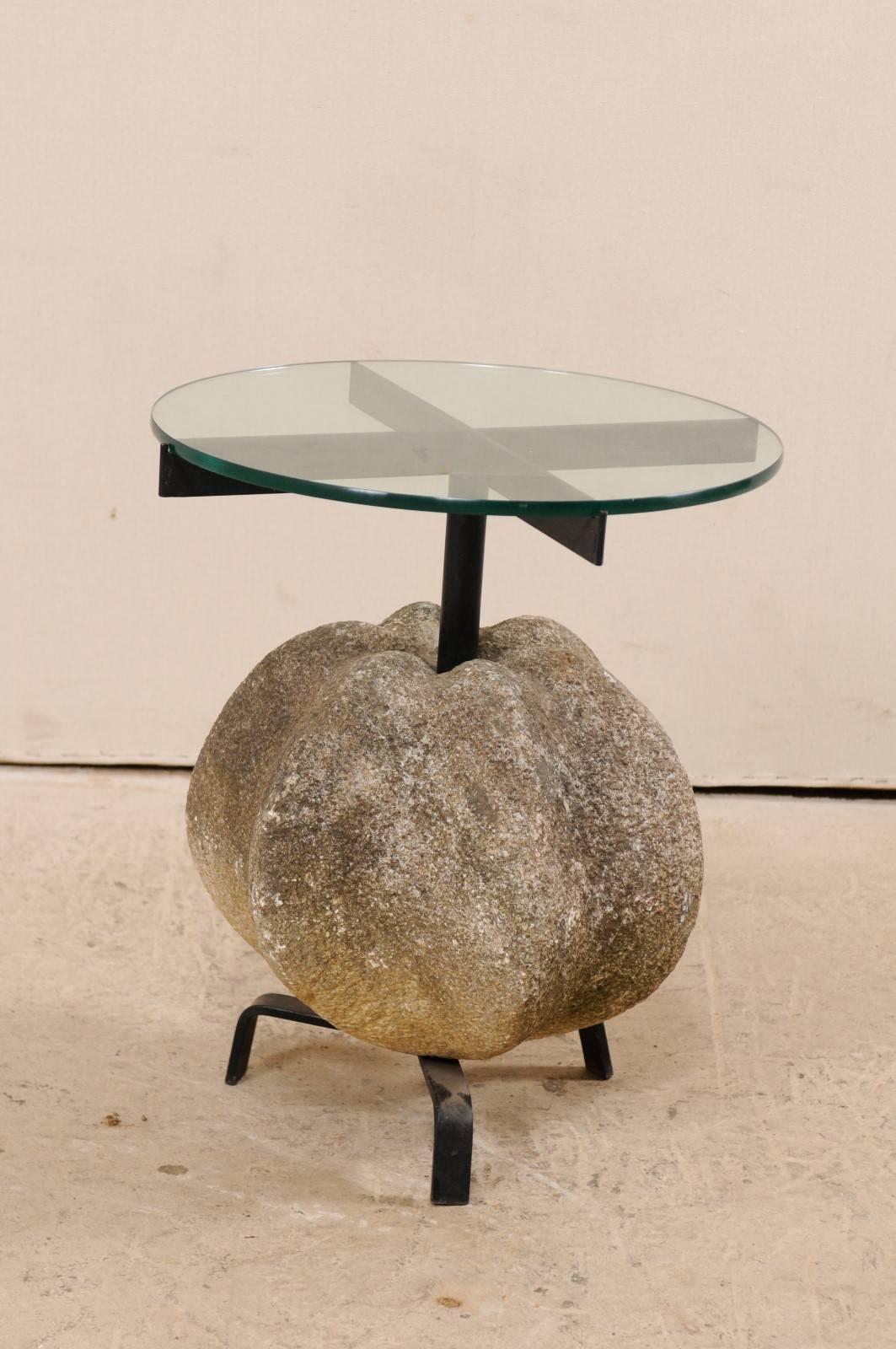 A custom antique stone and glass top side table. This unique side or drinks table features a large antique, segmented sphere-shaped stone which has been mounted onto a custom iron pedestal style base with tripod feet, and a clear circular-shaped