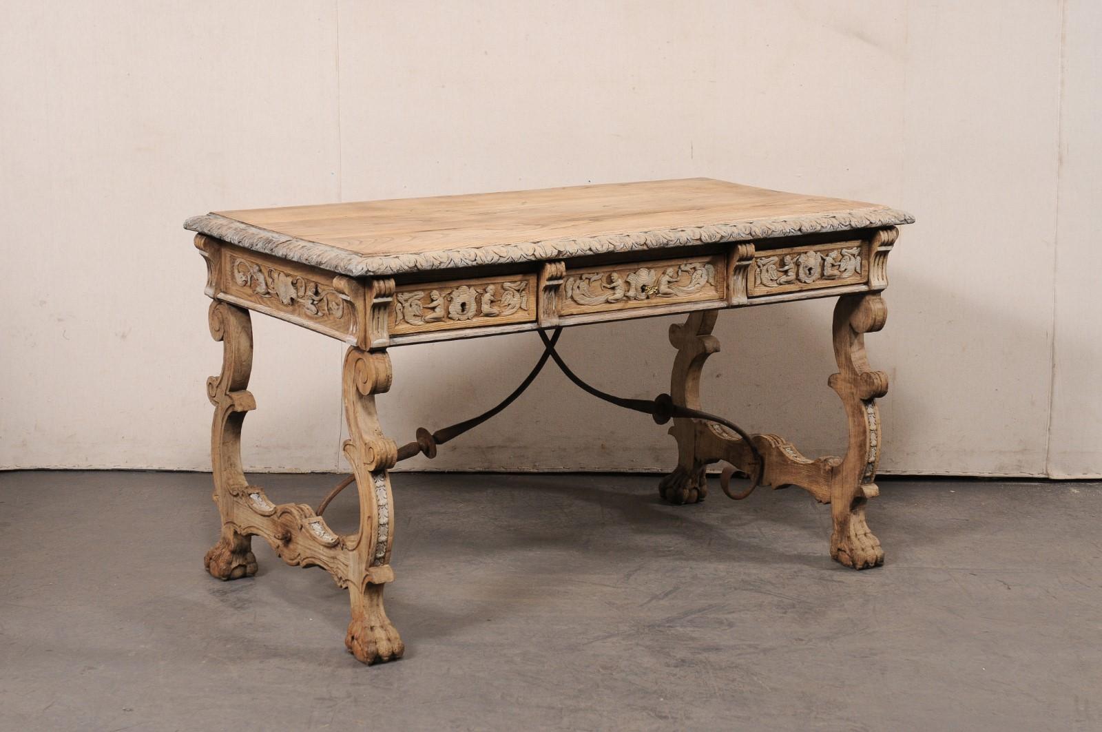 A Spanish elaborately carved wood desk, with trestle-legs and forged-iron stretchers, from the turn of the 19th and 20th century. This antique table from Spain has a rectangular-shaped top with leaf carved trim about the perimeter edges, which