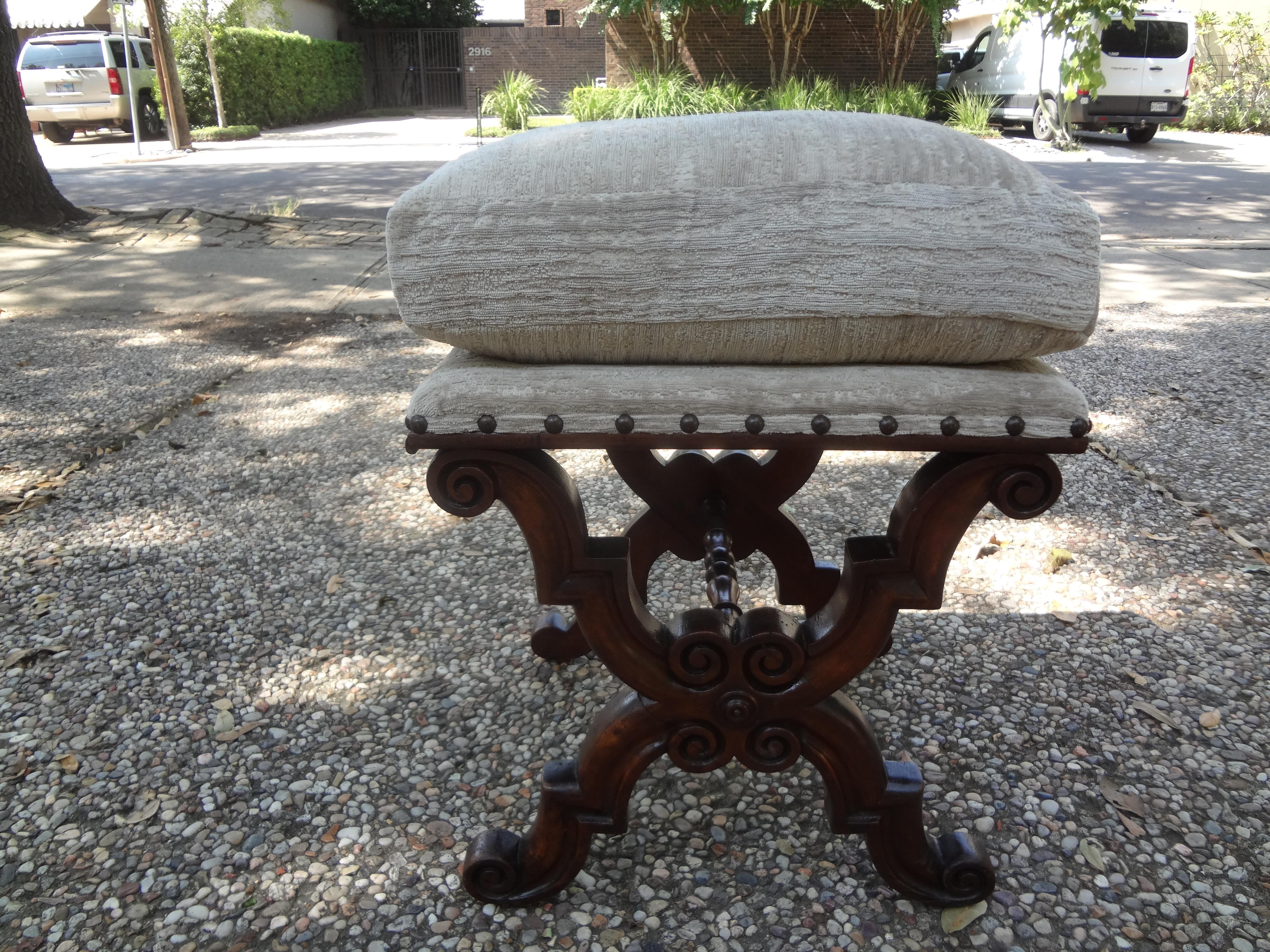 Gorgeous antique Spanish Renaissance style or Baroque style X-shaped carved walnut ottoman, stool or ottoman. This stunning bench is beautifully carved and dates to the 1920s. It has been newly upholstered in neutral chenille with spaced brass