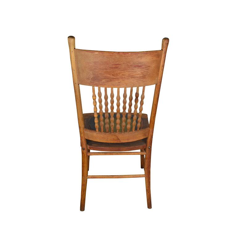 A beautiful antique carved wood chair with a leather seat. This unique piece features a tall wooden back with intricately carved floral detail at the top. The back features turned wood spindles at the center, with another bar at the bottom of carved