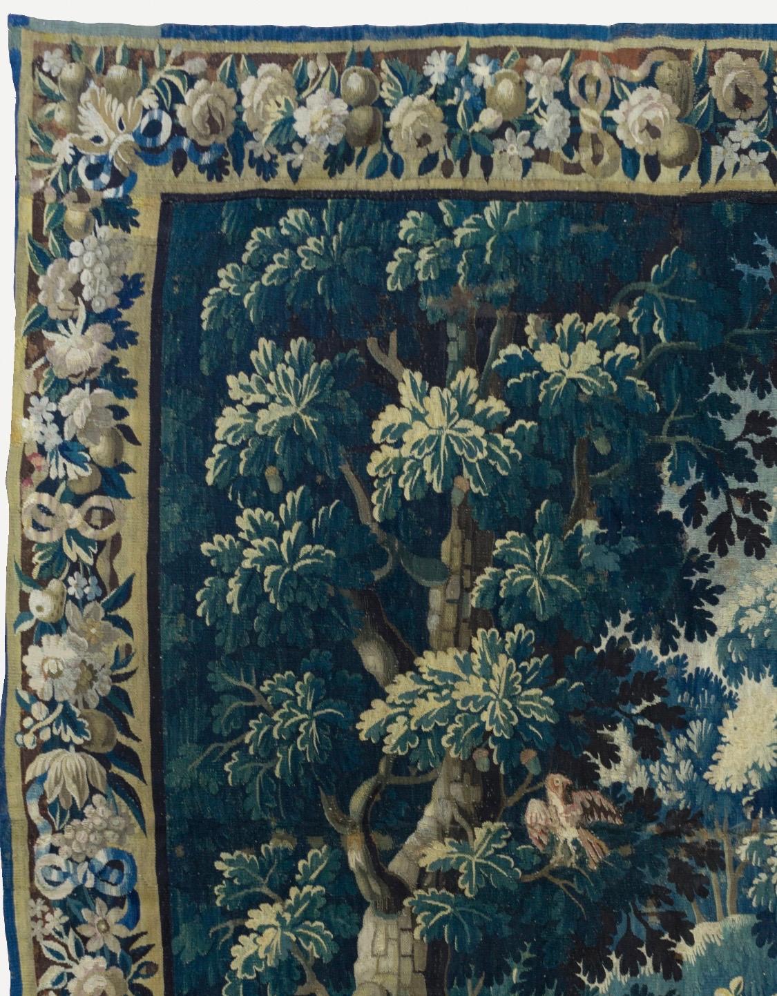 This is a gorgeous antique square 17th century flemish Verdure landscape tapestry with birds depicting a beautiful and rich summer scene of a countryside with lush trees and vegetation, birds and ducks and homes in the distance. The border features
