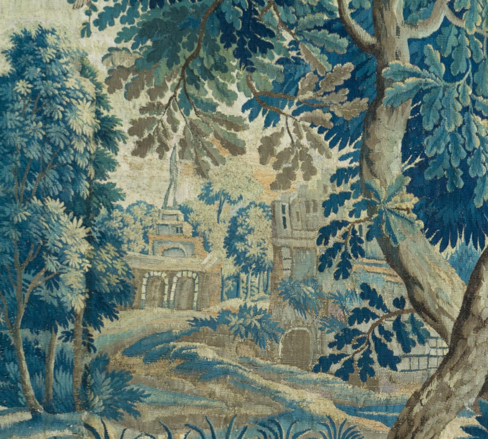 This is a gorgeous antique square 18th century flemish verdure landscape tapestry with birds depicting a beautiful and rich summer scene of a countryside with lush trees and vegetation, roosters, birds feeding their young, and homes in the distance.