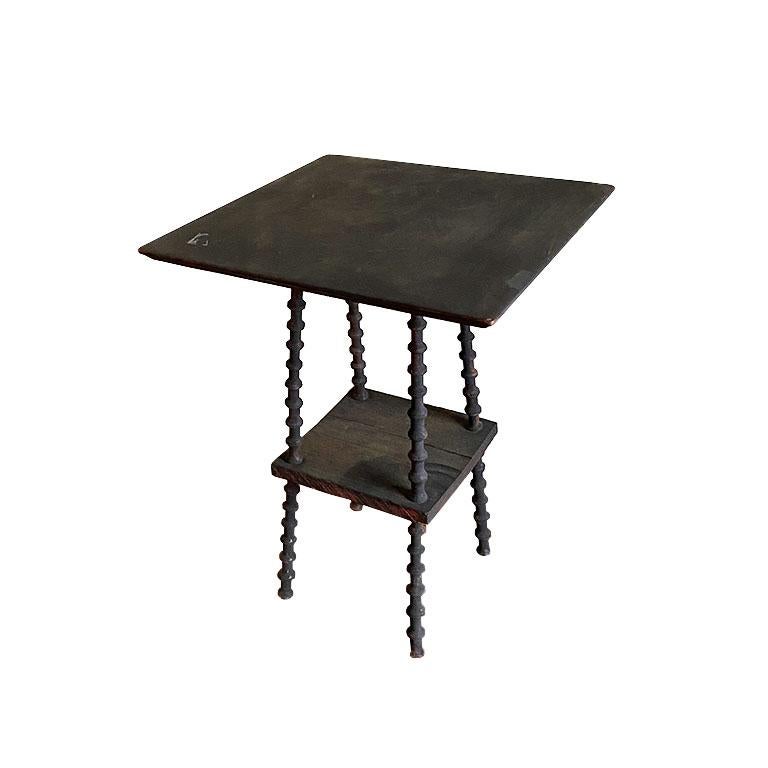 A small square wood tramp art style spool side table. This table is created from wood, and very old. It features a square top and square bottom shelf. Its legs are made from carved 
