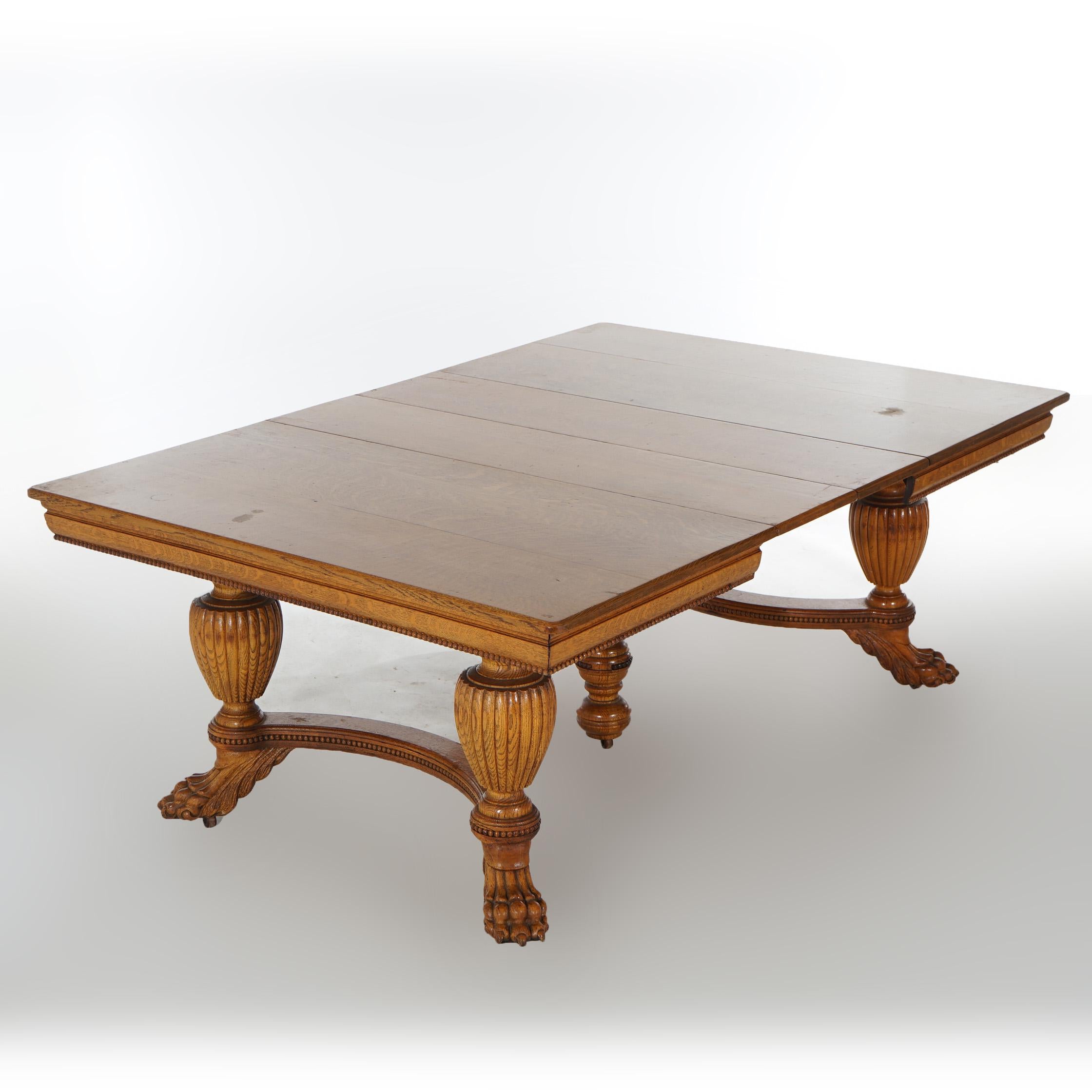 An antique square extension dining room table offers quarter sawn oak construction raised on urn form legs termination in oversized carved claw feet; includes two 11