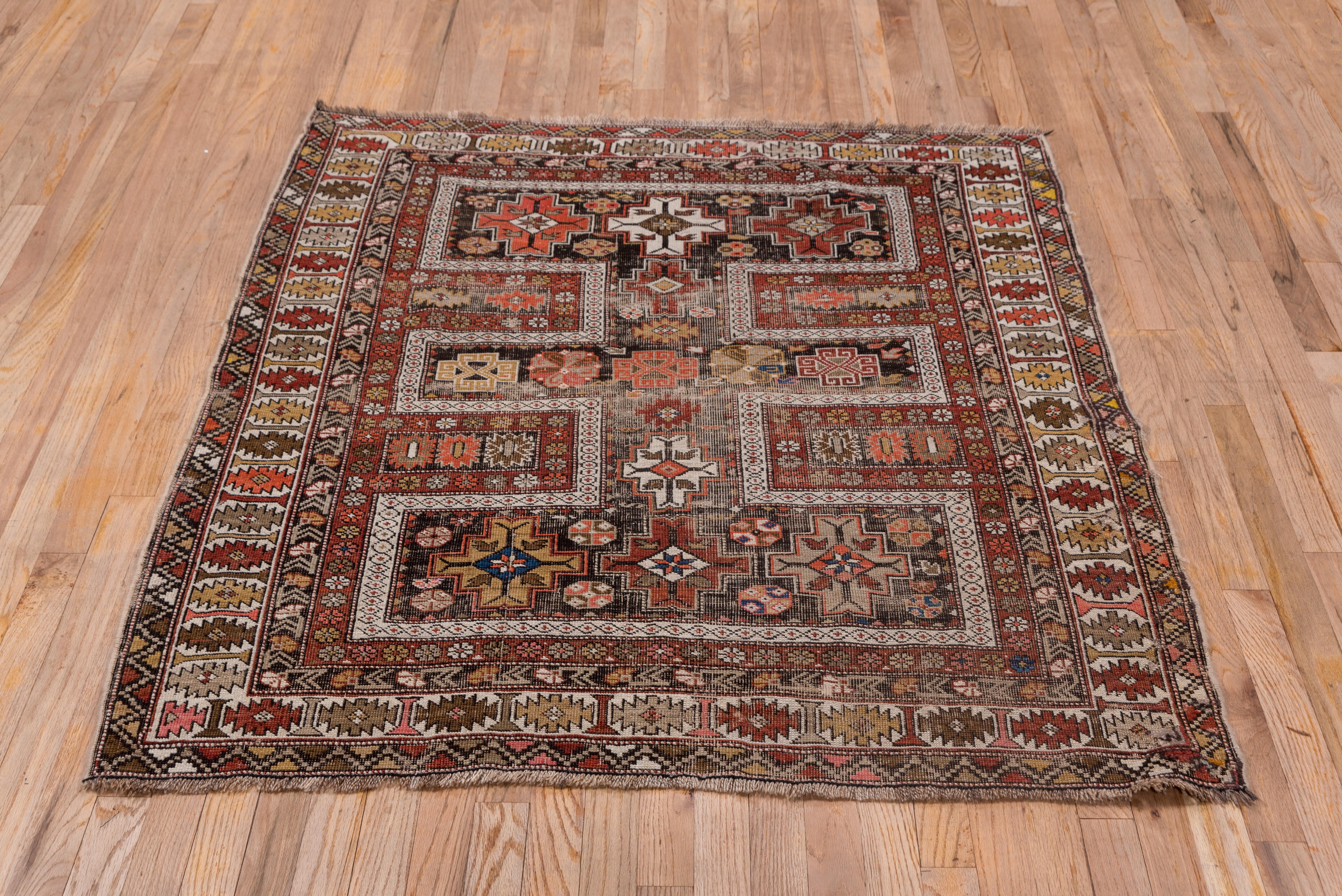 This well-filled east Caucasian rug shows a barred H pattern in ecru, enclosing stepped cross motives in brown-red, straw and pale blue all set on a brown-red grolund. The main ivory border features an ashik chain.