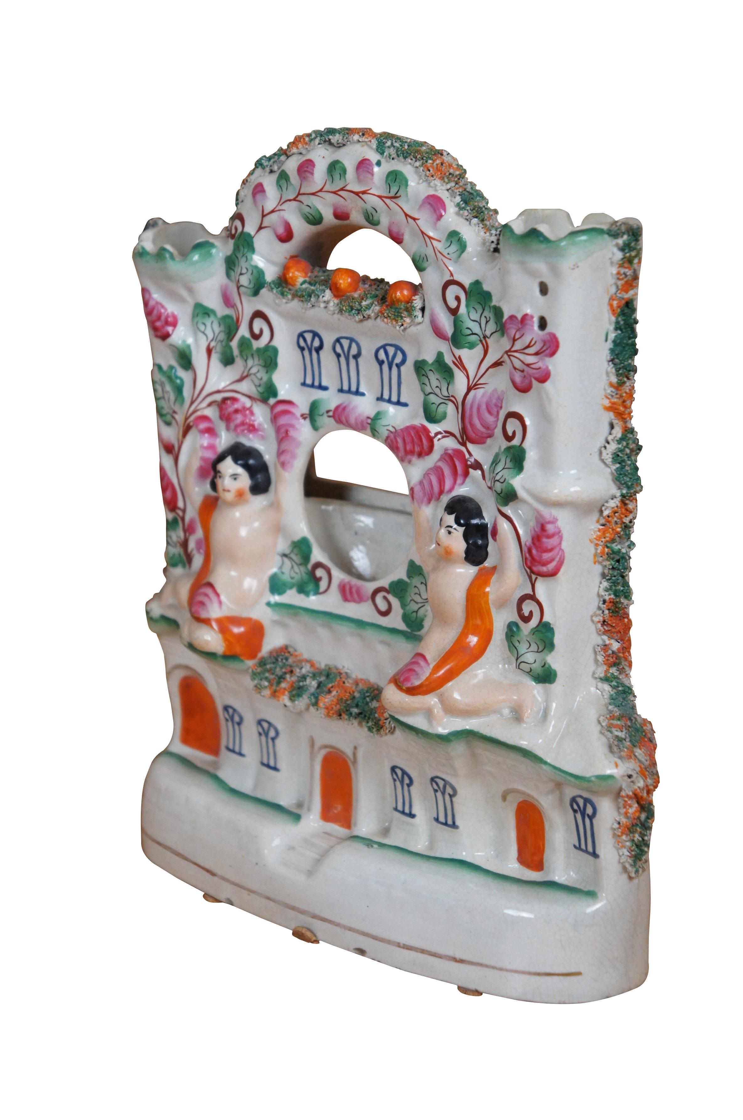Antique 19th century English Staffordshire porcelain flatback figurine in the shape of a castle / manor house covered in flowering vines and a pair of cherubs flanking the cup shaped section for displaying a pocket watch for use as a table clock.