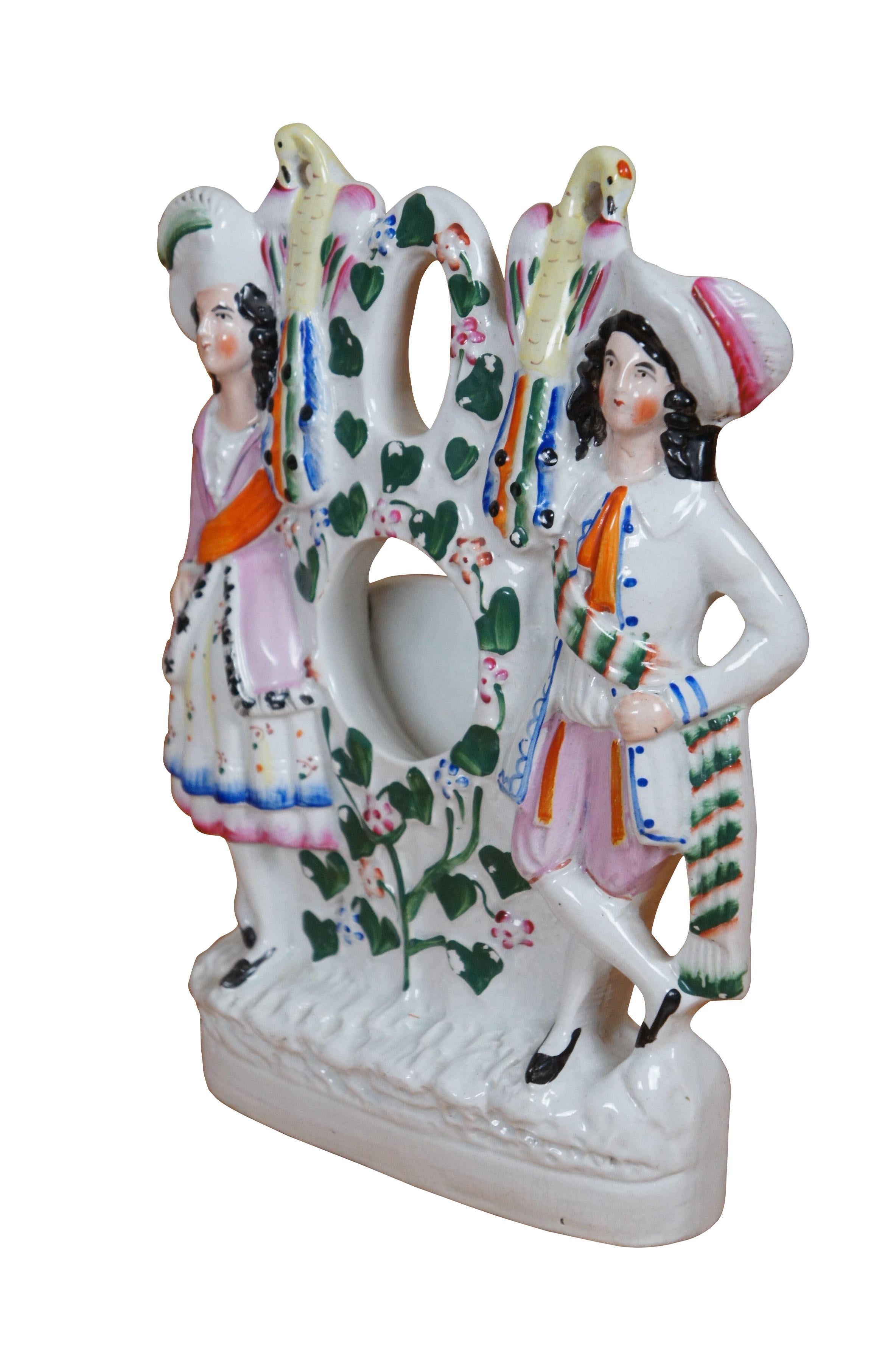 Antique 19th century Staffordshire porcelain flatback figural mantel pocket watch holder, allowing a pocket watch to be used as a table clock. Depicts a pair of figures in colorful clothing with peacocks on their shoulders standing in a