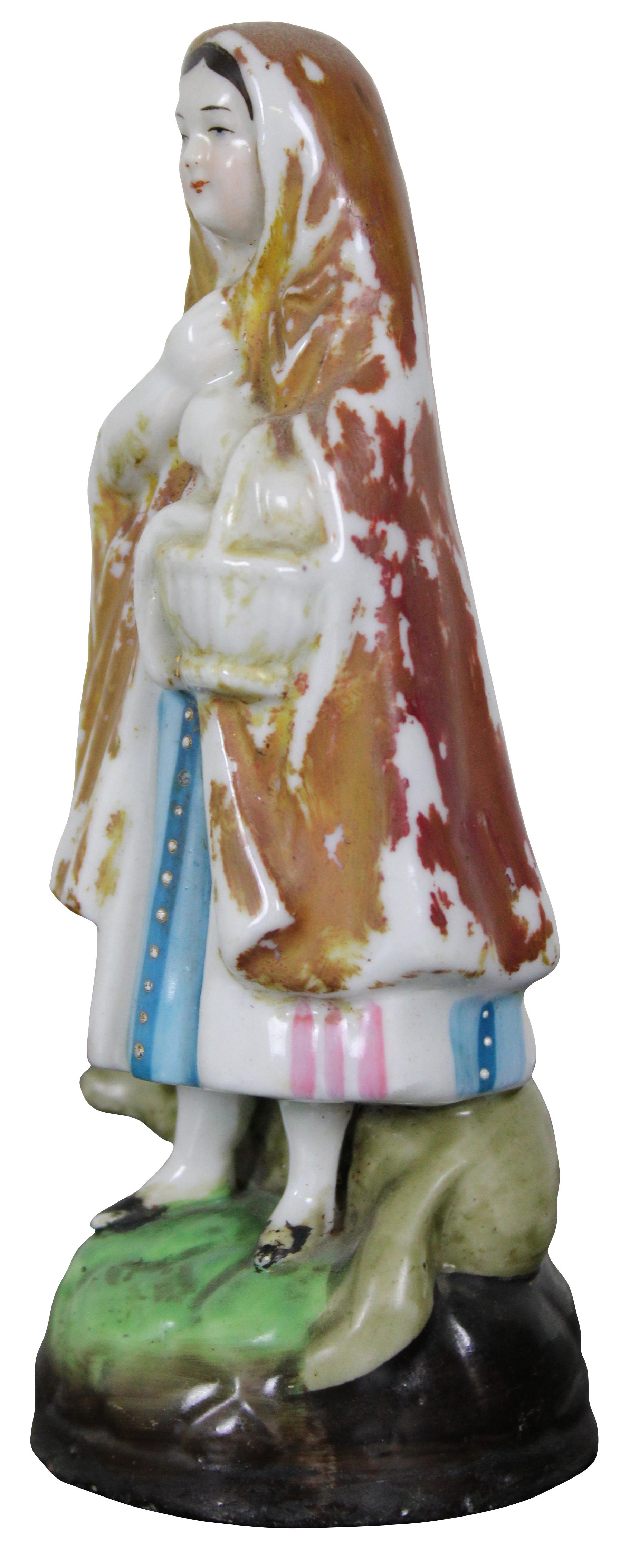 Antique 19th century miniature Staffordshire porcelain figurine of a peasant woman (Red Riding Hood) wrapped in a cloak, holding a basket, with a wolf at her feet.
 