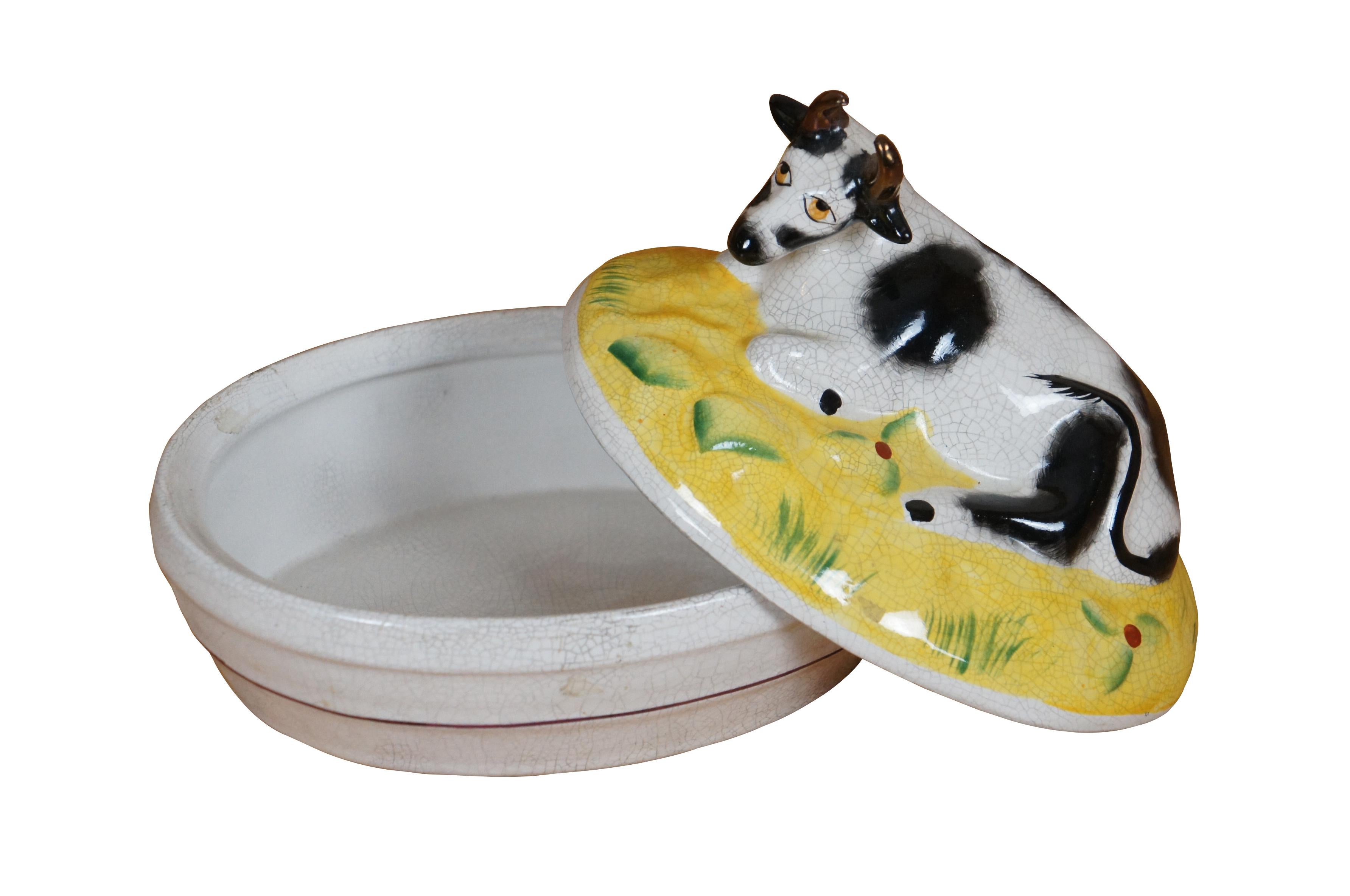 Antigua mantequera / baratija ovalada con tapa de porcelana de Staffordshire que representa una escena de granja con una vaca moteada en blanco y negro recostada sobre un campo amarillo.  Precioso ejemplar, de hacia 1868.

Dimensiones:
6,75