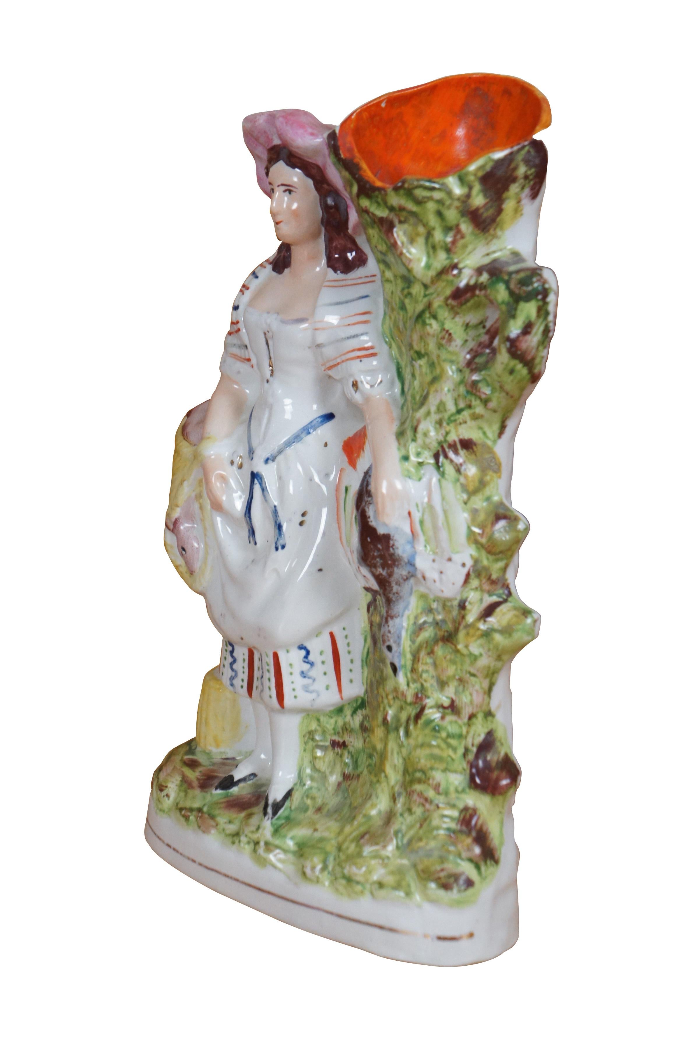 Antico vaso in porcellana Staffordshire del 19° secolo, con fondo piatto, raffigurante una giovane donna che trasporta della selvaggina.  un coniglio e un fagiano - accanto a un albero.

Dimensioni:

6,5
