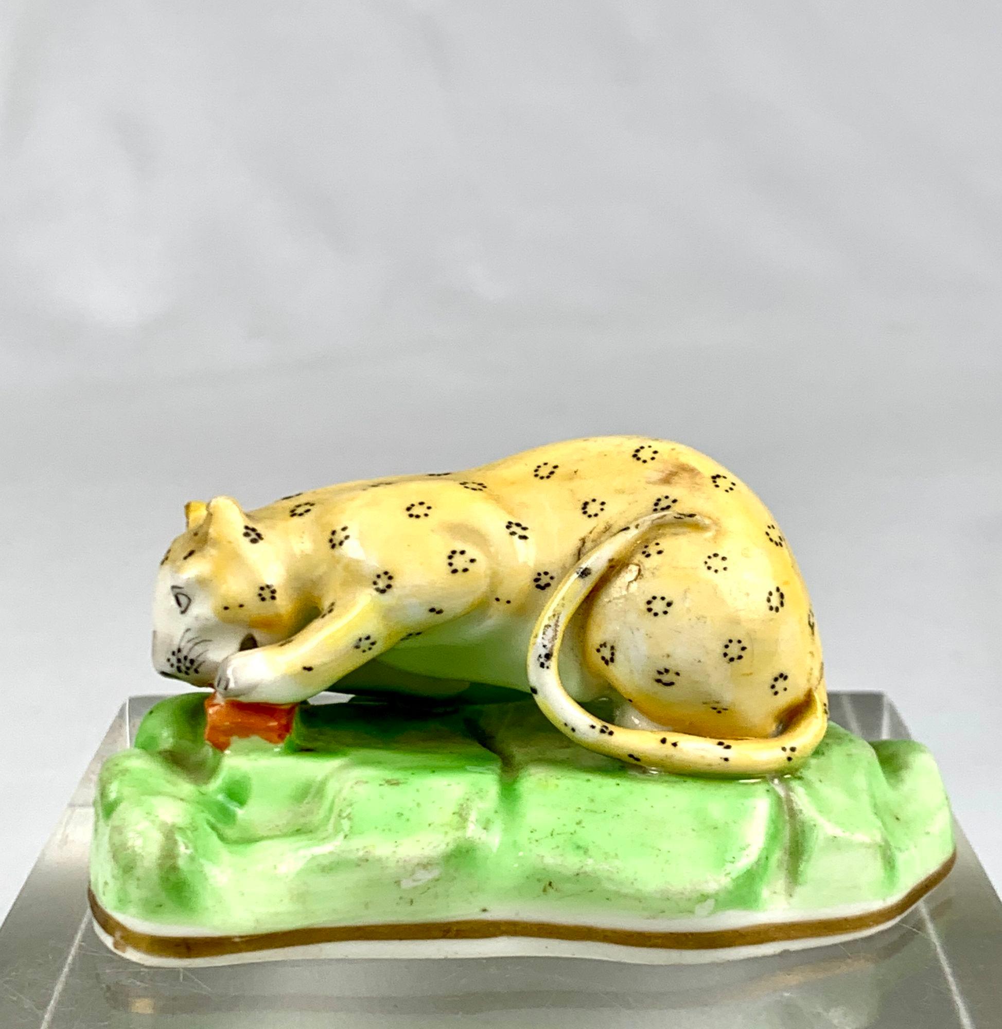 Diese antike Porzellanfigur eines Leoparden ist klein, aber wild.
Er ist mit einem Stück Fleisch im Maul auf einem felsigen Sockel liegend modelliert, der in Grün gehalten und mit einer vergoldeten Linie eingefasst ist.
Das Fell des Leoparden ist