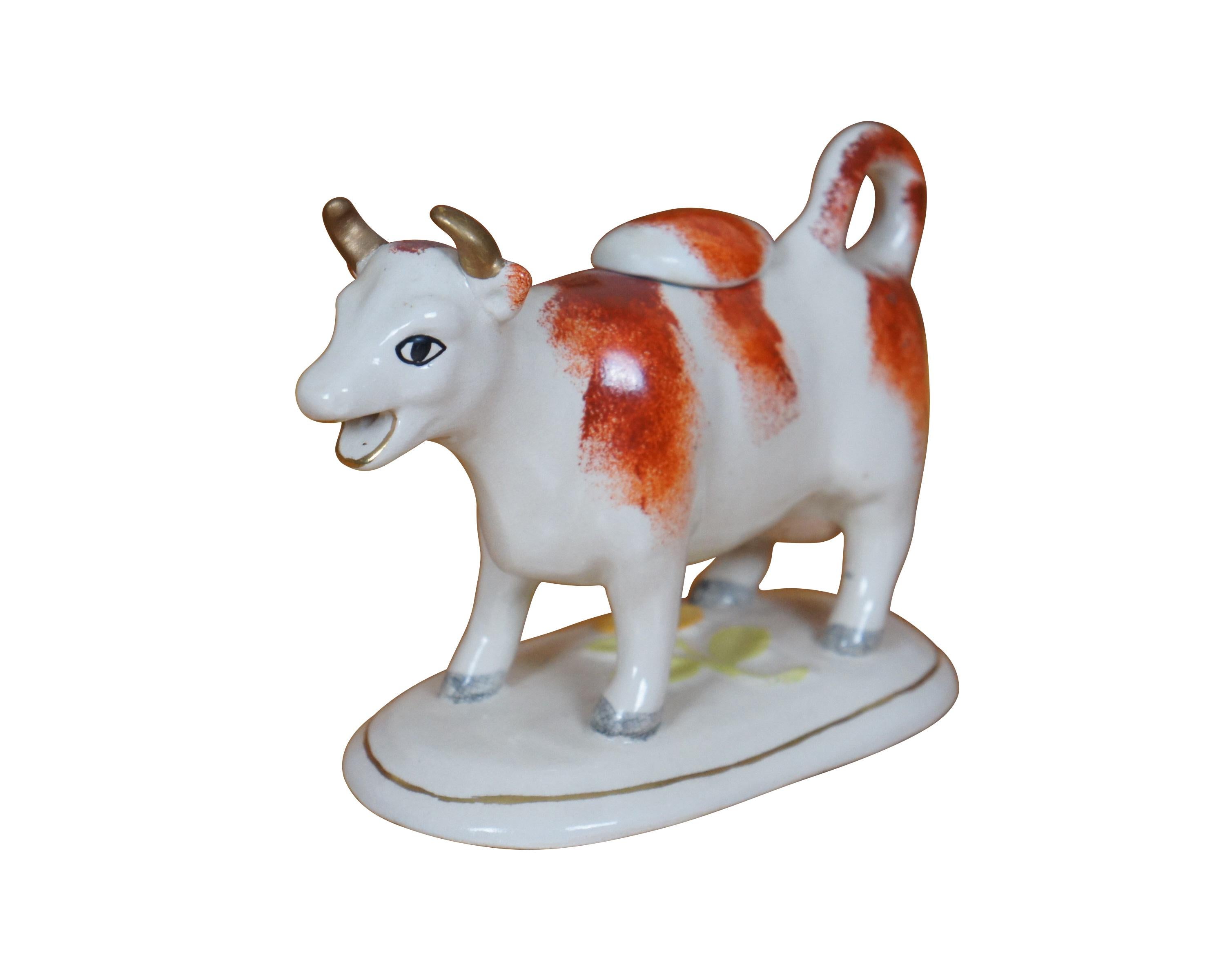 Antiker Sahnekrug aus Staffordshire aus dem 19. Jahrhundert in Form einer rot-weißen Kuh auf einem ovalen Sockel, geformt und bemalt mit einem gelben Gänseblümchen. Der Schwanz rollt sich zu einem Griff zusammen. Vergoldete Hörner. Inklusive