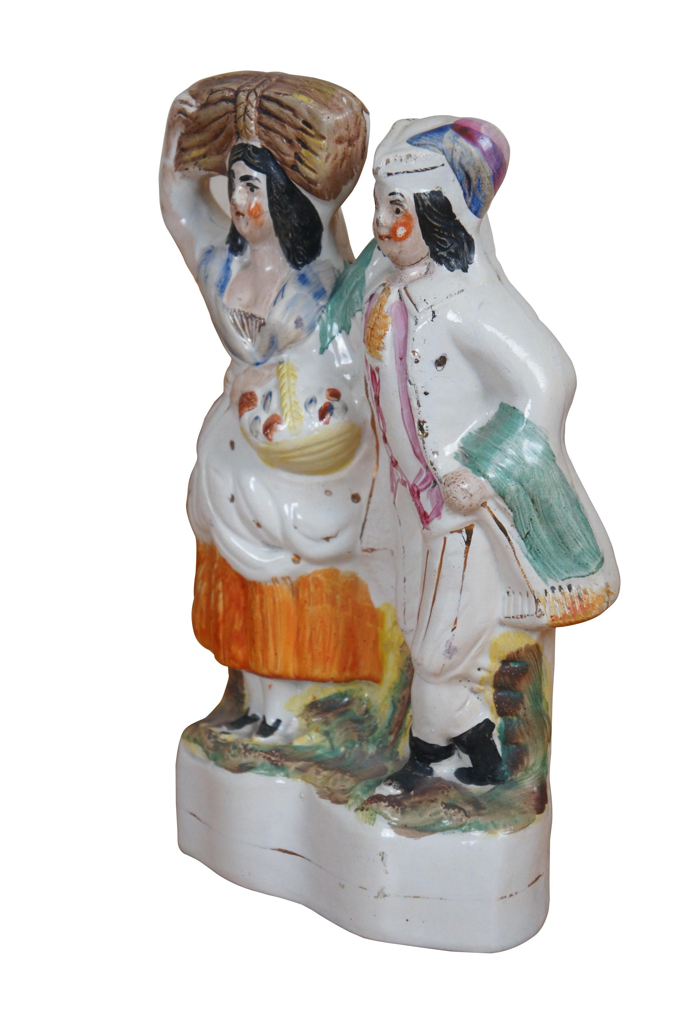 Antigua figurita de porcelana plana de Staffordshire del siglo XIX que representa a una pareja de figuras: un caballero con ropas finas y el brazo alrededor de la cintura de una mujer que lleva una cesta de productos y un haz de paja en la