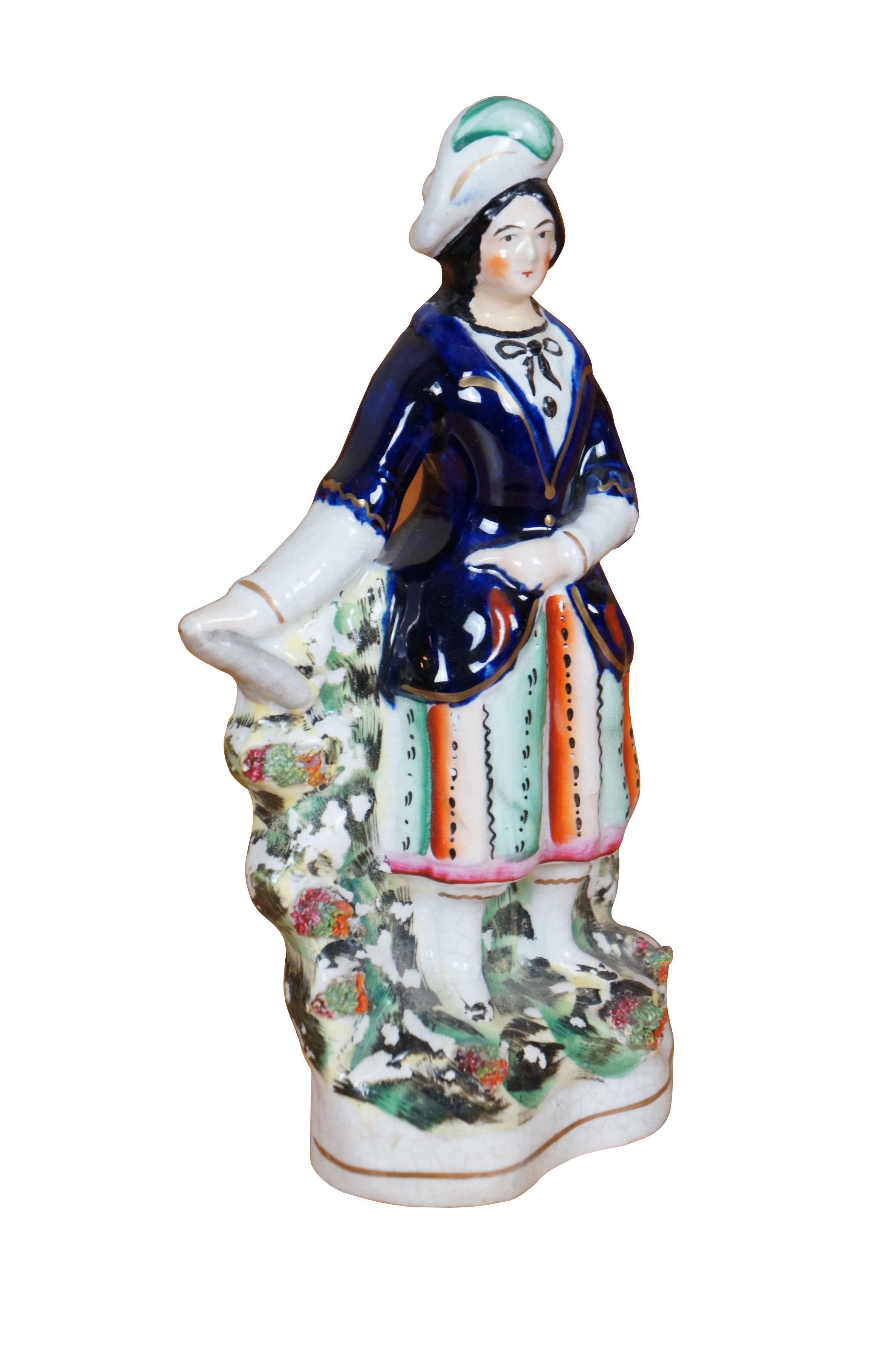 Antica statuetta in porcellana Staffordshire del XIX secolo raffigurante una donna pastore scozzese highlander con cappello piumato, giacca blu cobalto e gonna da equitazione verde e arancione, su un motivo floreale muschiato.

Dimensioni:
4,25