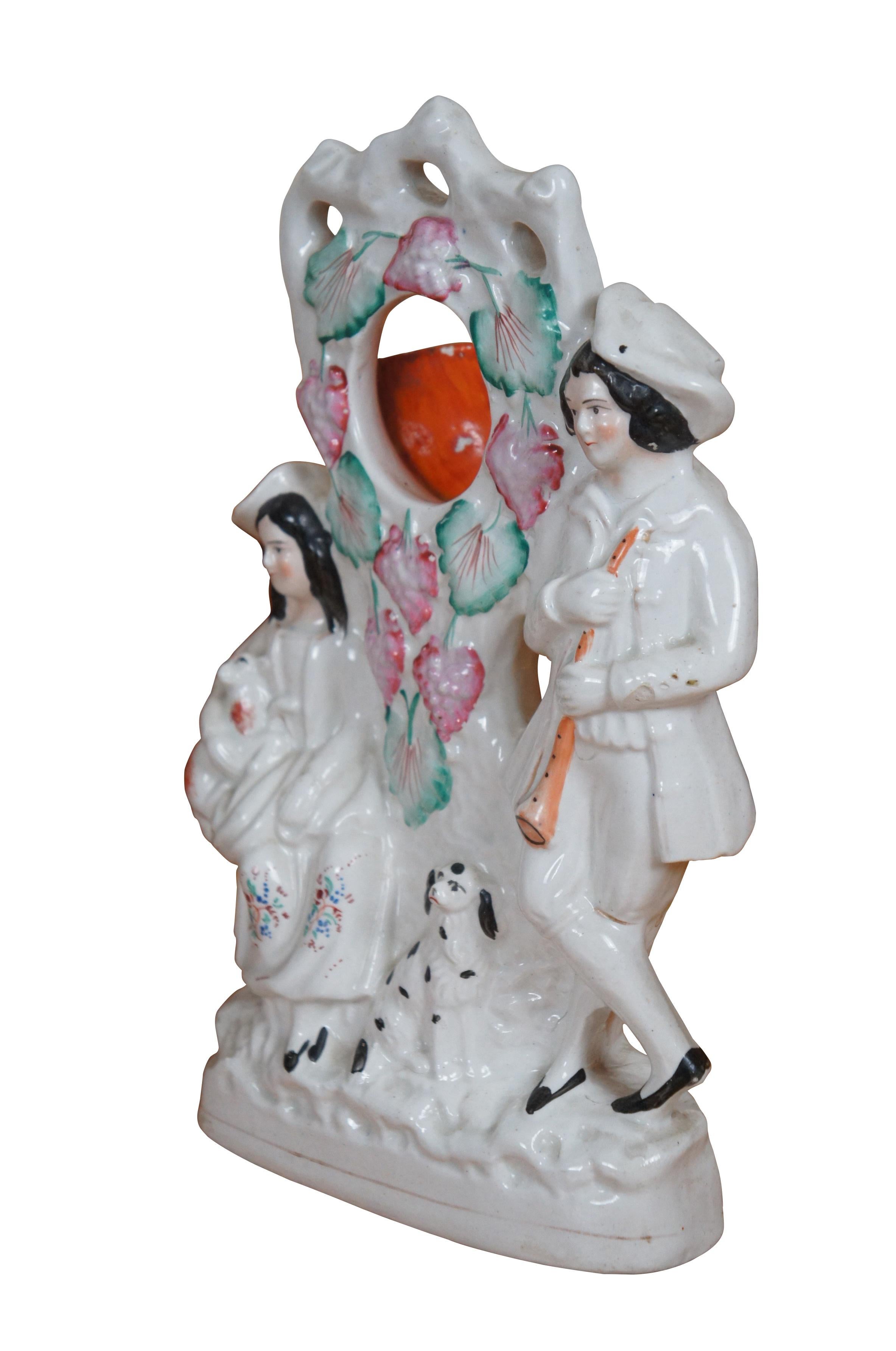 Antique 19th century Staffordshire porcelain flatback mantel figurine designed with a cup shaped section to hold a pocket watch, allowing it to serve as a table clock. Figure depicts a shepherd with a flute and shepherdess holding a lamb on her lap,