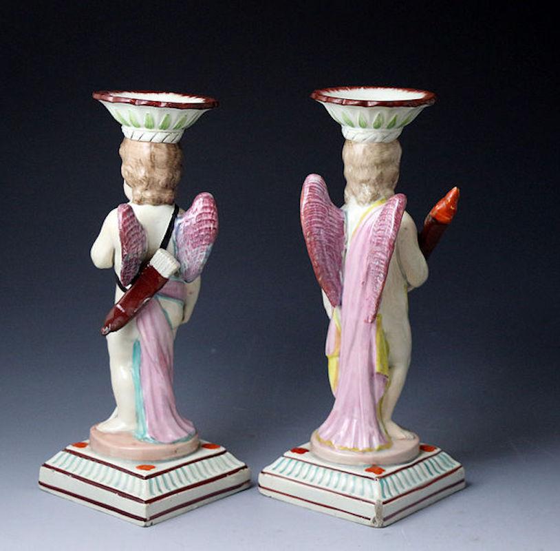 A pair of classically inspired Staffordshire pottery candlestick figures of Cupid and a Putti holding a flaming torch. 
This quality pair are finely modeled and painted and date to the latter 18th century period. 
A good decorative
