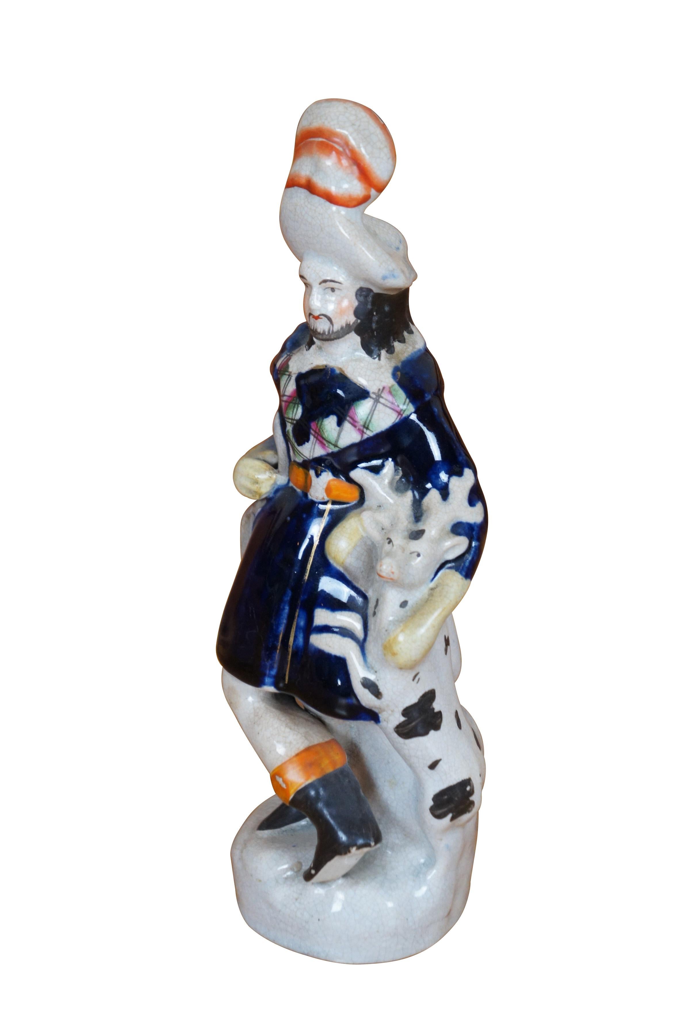 Ancienne figurine à dos plat en porcelaine du Staffordshire du 19ème siècle représentant un  Chasseur écossais en veste bleu cobalt bordée d'écossais, tenant son arc et saluant un cerf noir et blanc.

Dimensions :
3,5