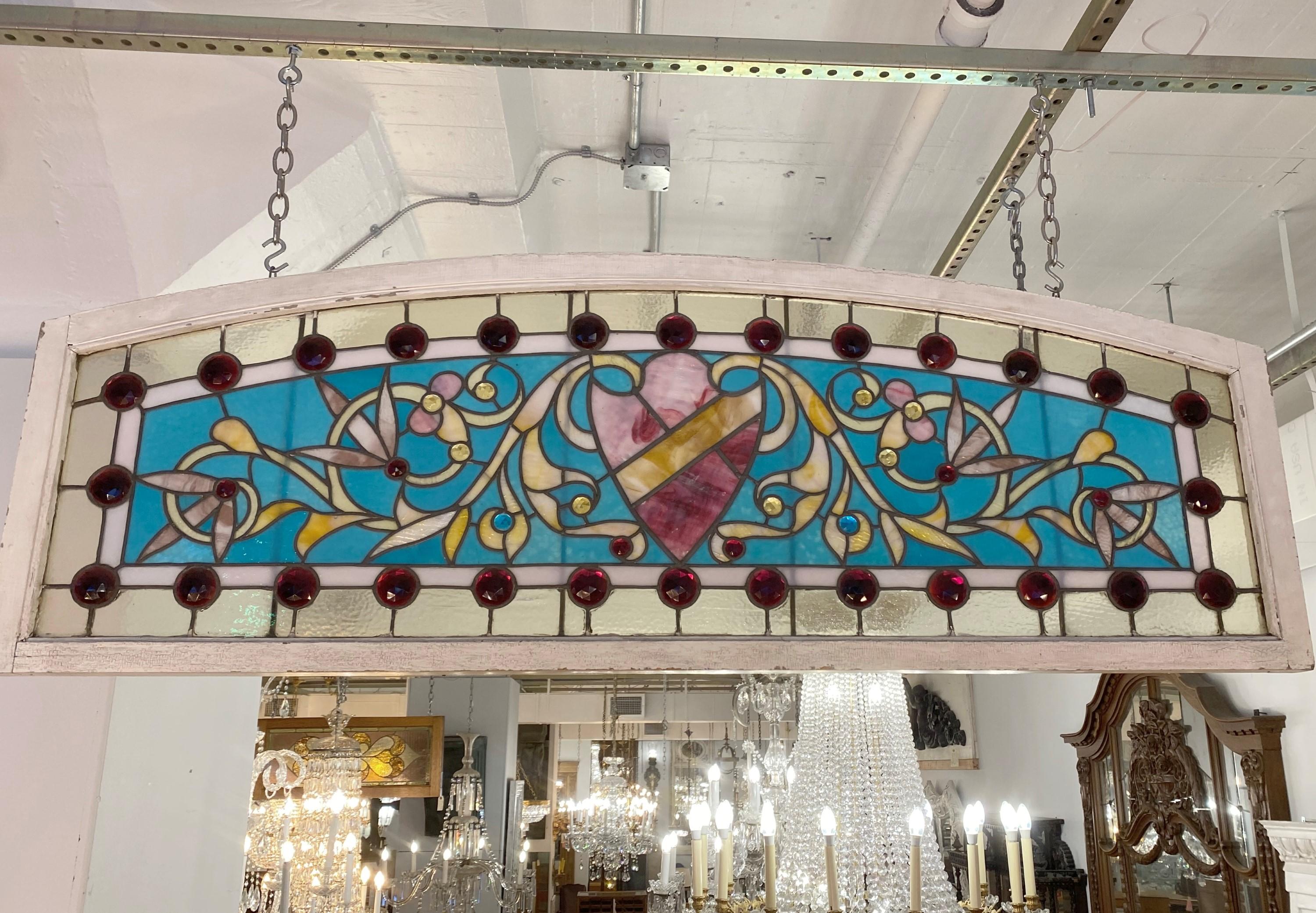 Early 1900s arched stained glass transom window. The wide width and highly ornate design shows this was part of an over the top entranceway. The large center shield is flanked by smaller jewels in vivid red, yellow and blue colors. Please note, this
