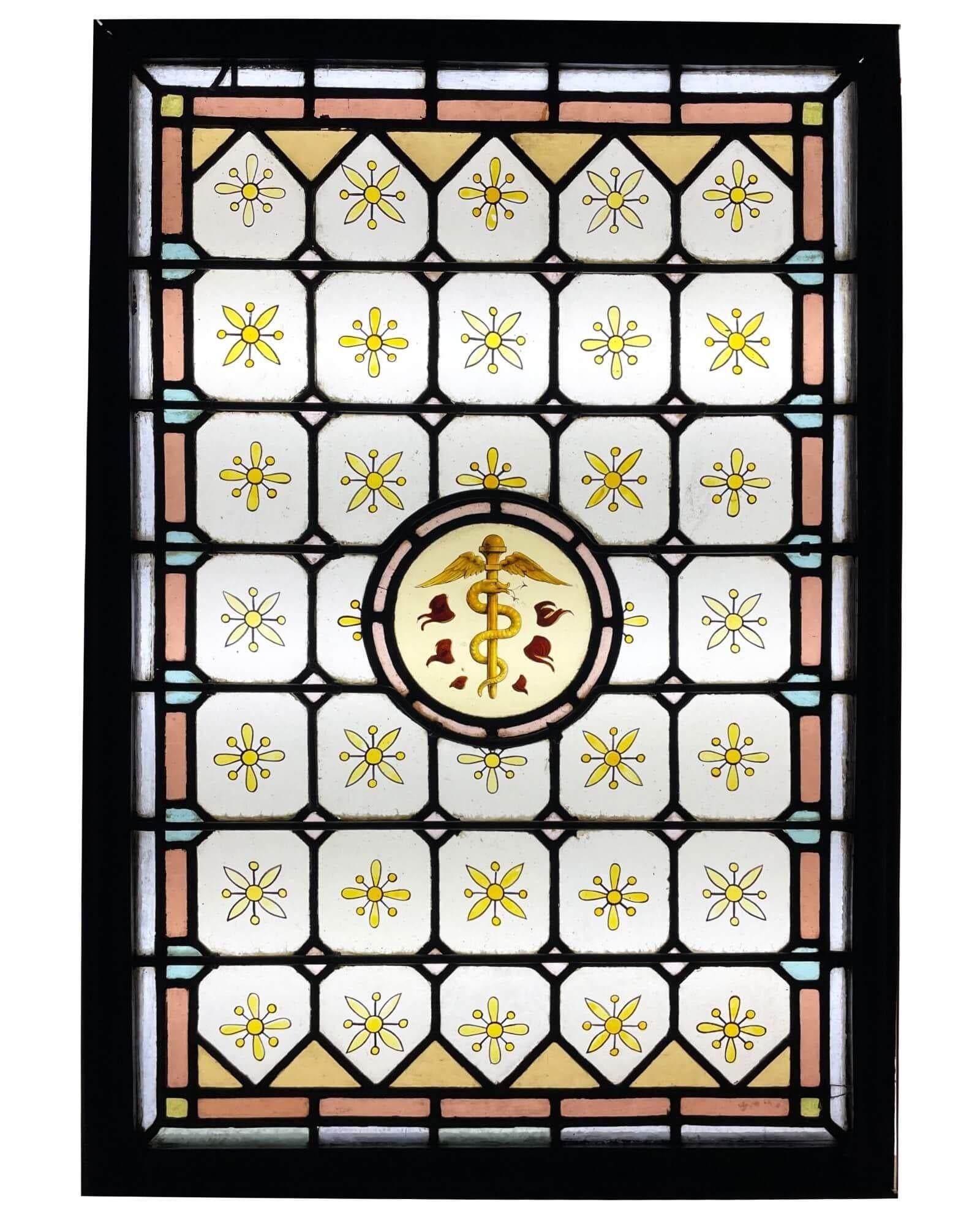 Ein antikes Glasfenster aus dem späten 19. Jahrhundert mit der Darstellung des griechischen Äskulapstabs, dem Symbol der Gesundheit und der wissenschaftlichen Medizin. Es stellt eine Schlange dar, die sich um einen Stab mit Engelsflügeln an der