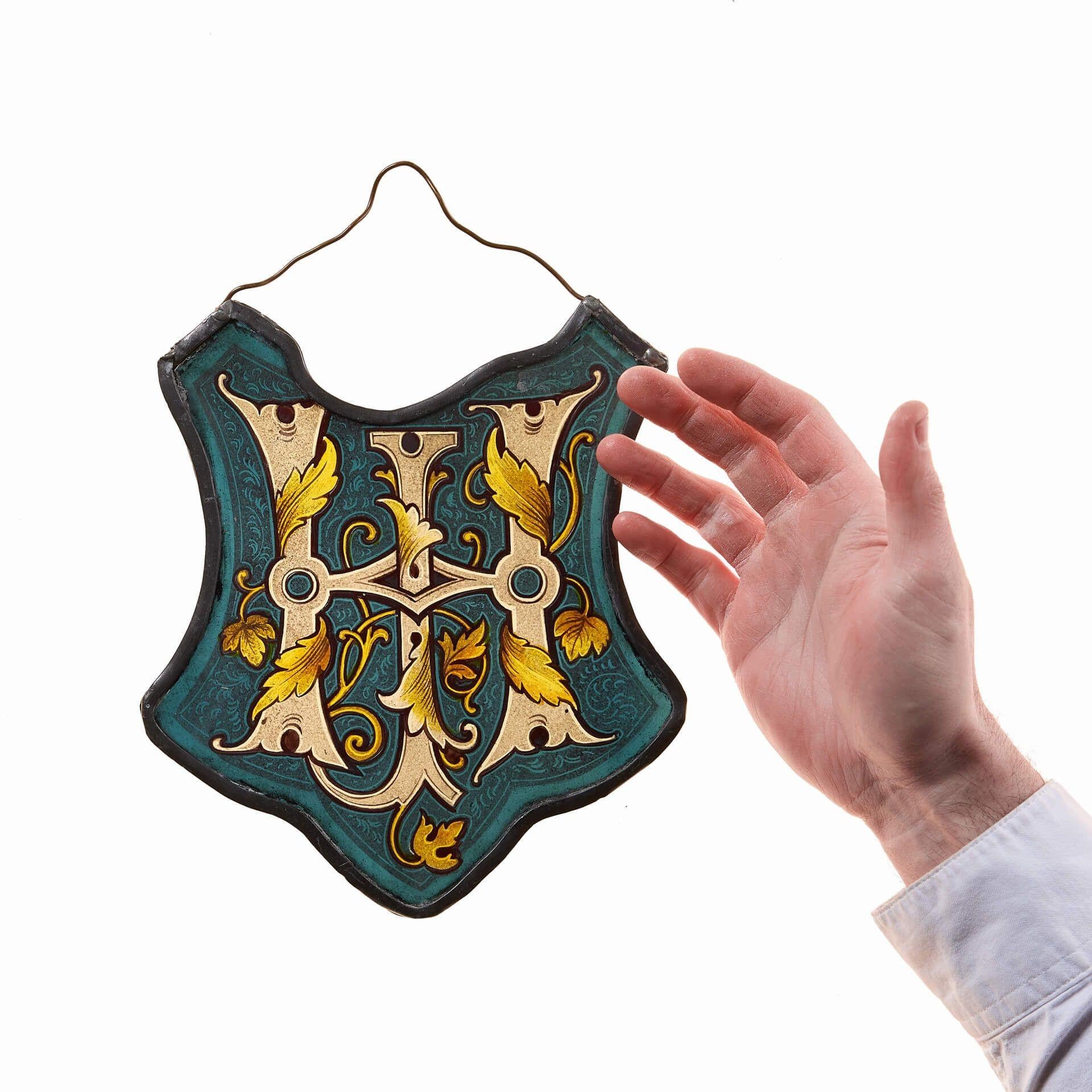 An antique stained glass shield baring the monogram 'HJ', dating to circa 1880.

Unusually shaped, this small stained glass panel uses a myriad of different coloured glass panes and patterns certain to catch the eye.

A blue ground with foliage in