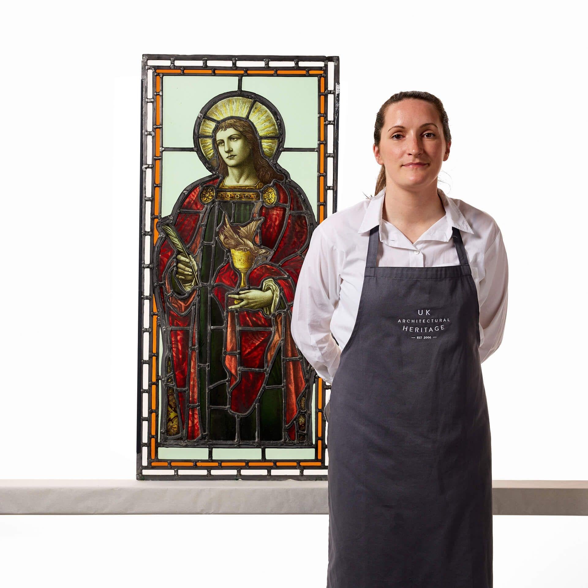 Una gran e impresionante vidriera antigua que representa a San Juan Evangelista y que data de hacia 1860. En esta asombrosa pieza de cristalería, el Santo está representado con un vibrante ropaje rojo, una pluma en una mano -que representa su papel