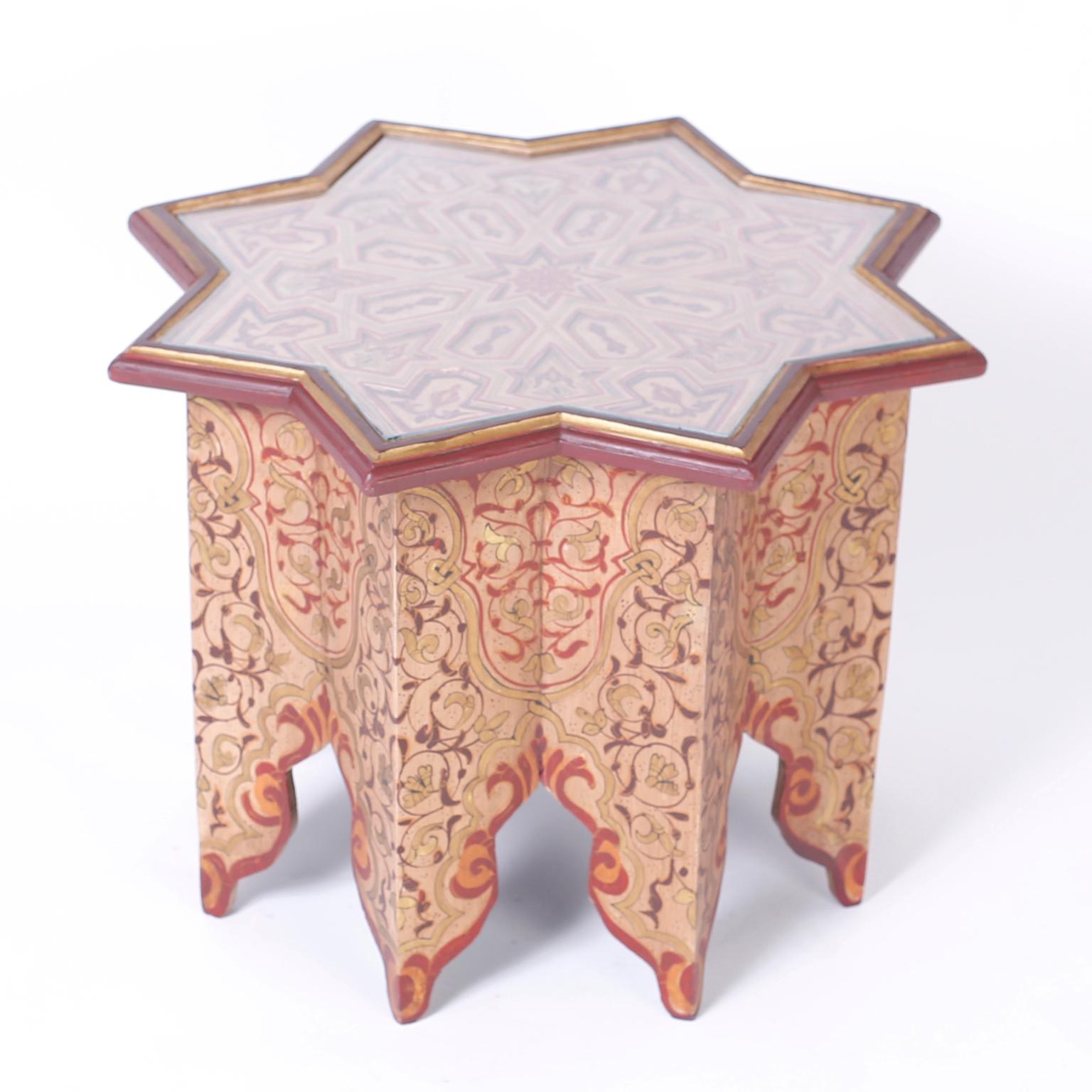 Moroccan wood table or stand with a star form top with removable glass over inset geometric designs. The sixteen sided base is painted with floral decorations and features Moorish arched legs.