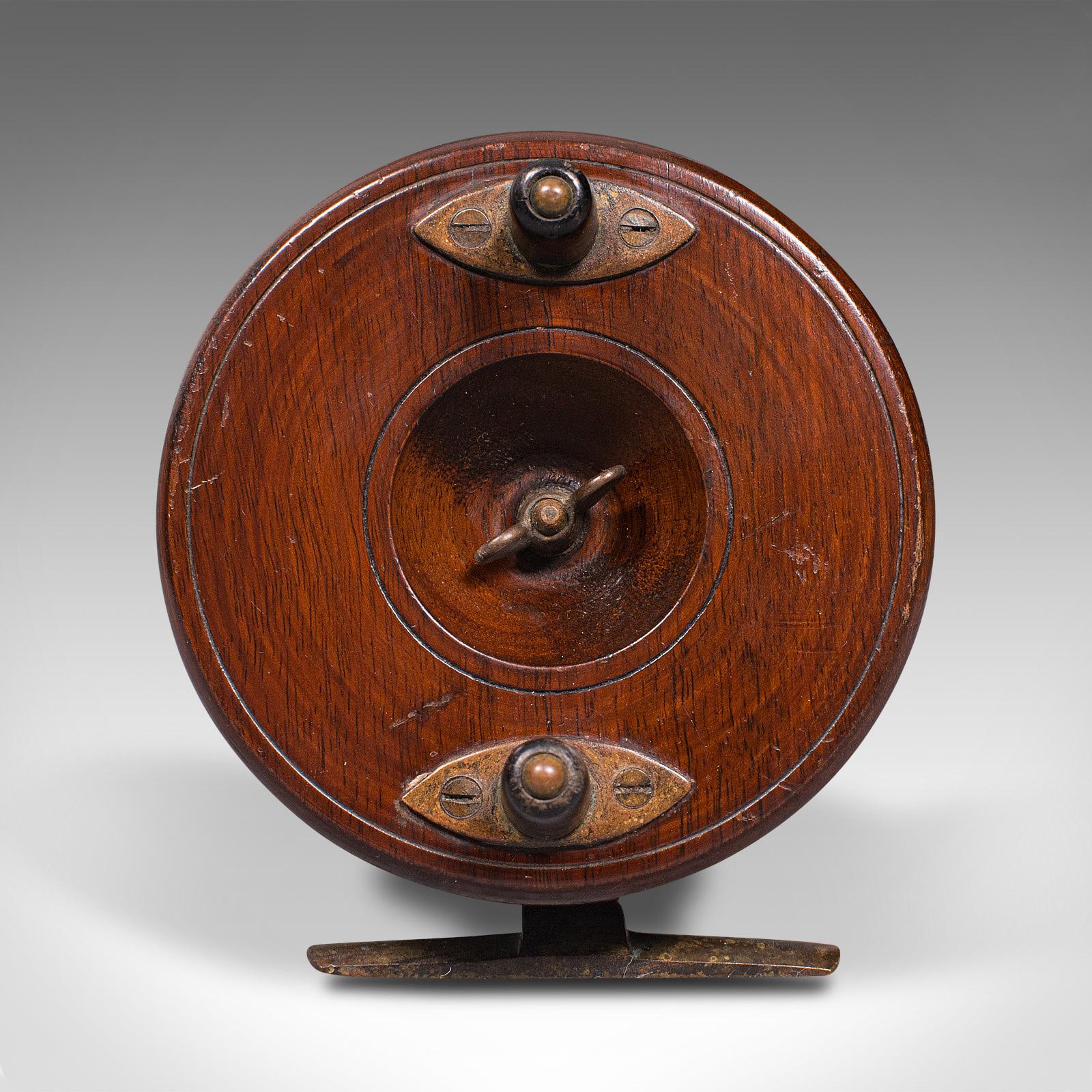 This is an antique starback fishing reel. An English, mahogany and brass decorative 4