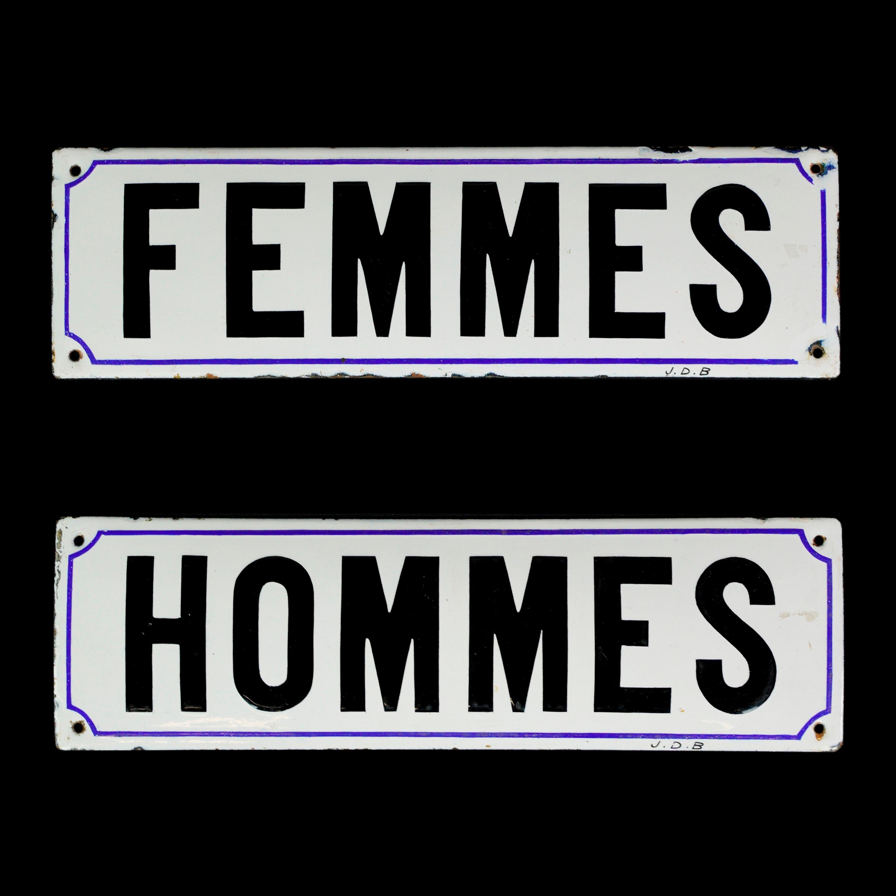 Enameled steel white signs with black lettering in French for men and women outlined in blue. Good condition with appropriate wear from age. Stamped J.D.B. Priced as a pair. Please note, this item is located in one of our NYC locations.