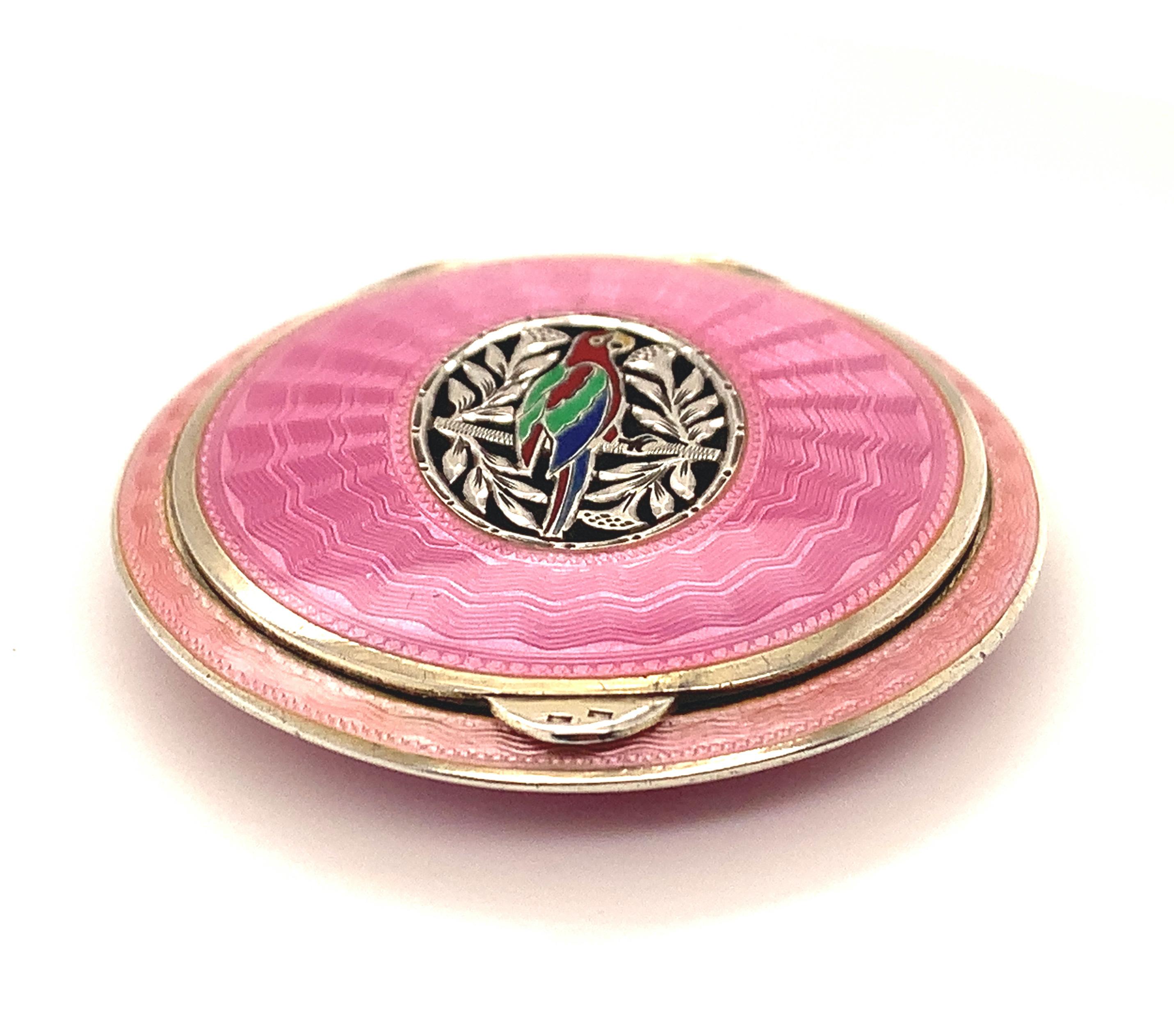 Bright and colorful hinged compact.  Pink guilloche enamel top and bottom.  There is a center cut-out cartouche with an enameled parrot.  2 1/8