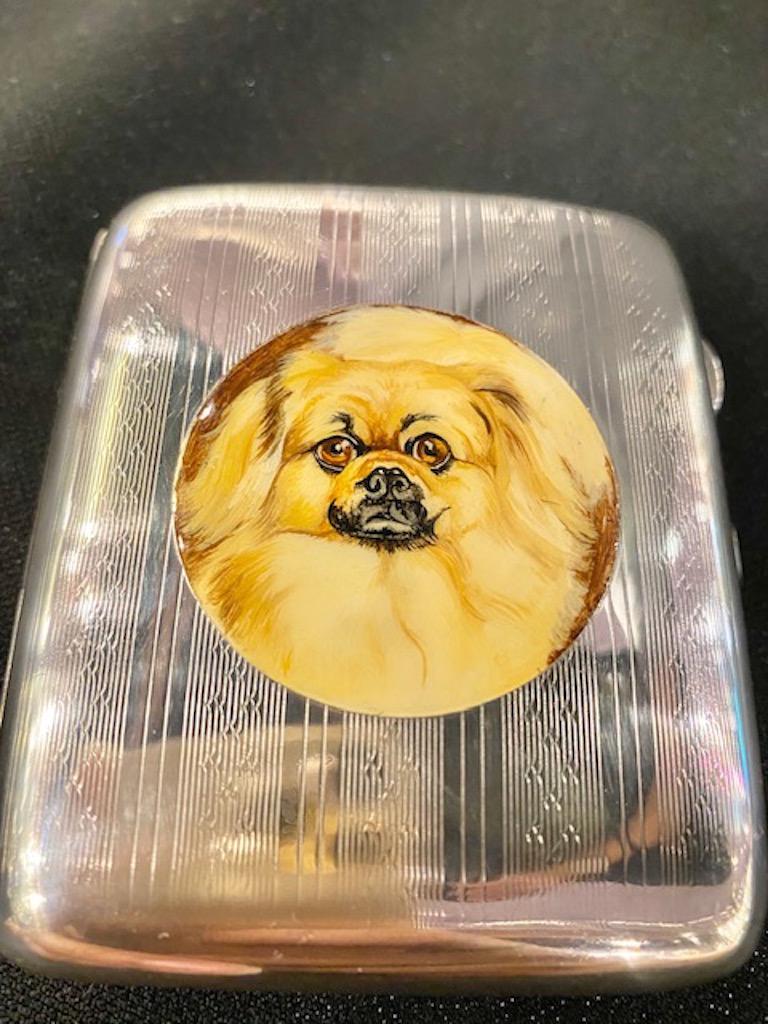 Very handsome sterling silver hinged case.  Allover finely detailed engine-turned pattern, front and back.  Set with a center cartouche of an enamel pekinese dog.  Portrayed in varying shades of beige, brown and black enamel.  Gilt interior.  Solid