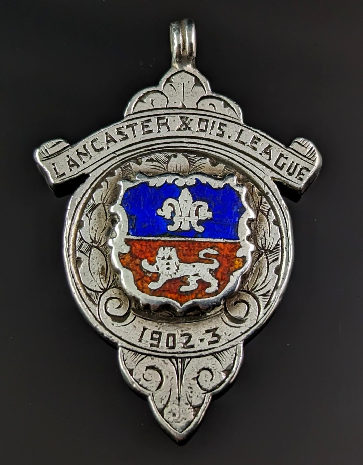 An attractive vintage sterling silver and enamel fob pendant.

It is an interestingly shaped piece with a central enamelled design in rich blue and red, highlighting a Fleur de Lis and a lion.

It reads Lancaster Dis. League, 1902 - 3.

The fob has