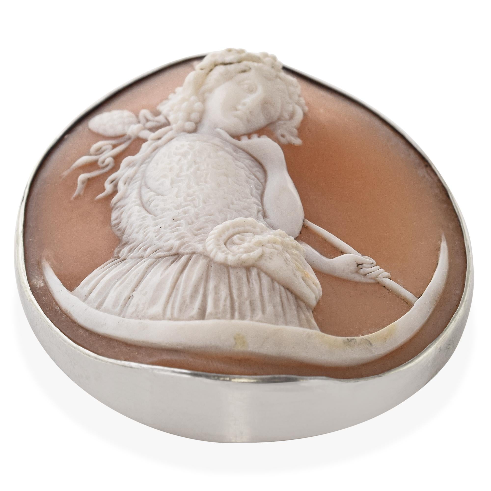 This vintage shell cameo brooch features a beautifully hand-carved classical woman seated beside a flowing urn, a scene that may represent Ariadne, the mythological figure known for her connection to love, loss, and renewal. The delicate carving