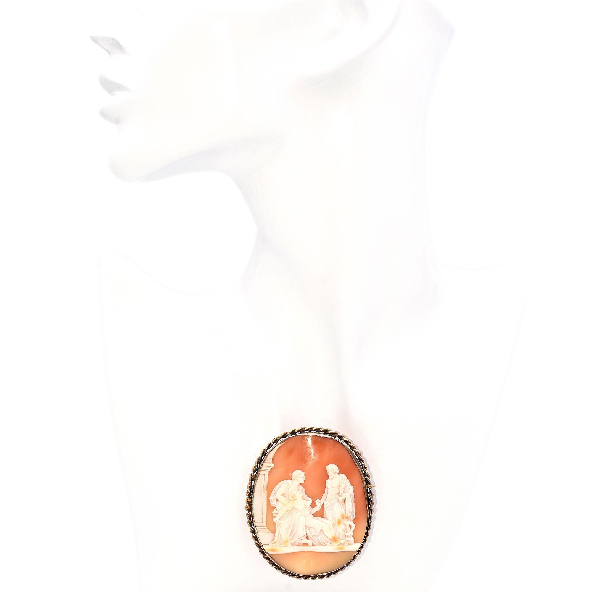 This antique brooch showcases a finely carved cameo depicting a classical scene with Asclepius, the ancient Greek god of medicine, healing, and physicians. He is often depicted, as he is here, holding a staff with a serpent coiled around it, which