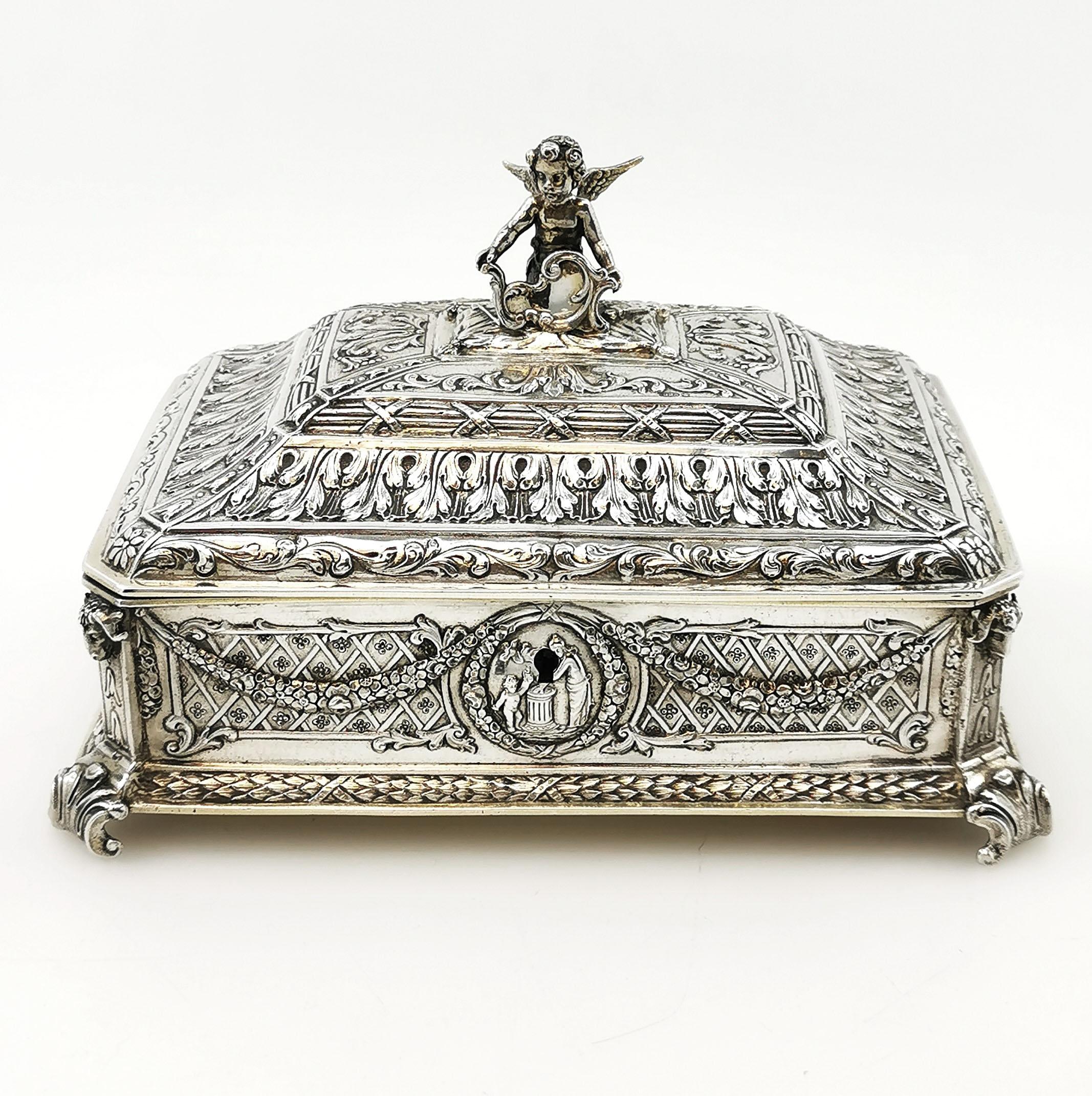 A lovely Antique sterling Silver Box suitable as a Jewellery Box or a trinket box. This lovely Box has an ornate chased design on its sides and stepped lid with a little cherub on the top as a finial. The Box stands on four stylised leaf feet and is