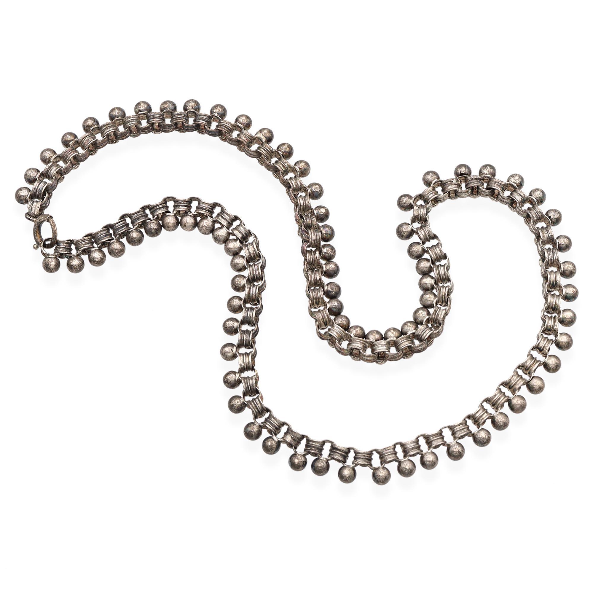 Questa collana è caratterizzata da una serie di piccole perle d'argento, distanziate in modo uniforme per tutta la lunghezza, che creano un motivo ritmico. Le perline sono collegate da maglie intricate che formano un disegno continuo ed elegante. La