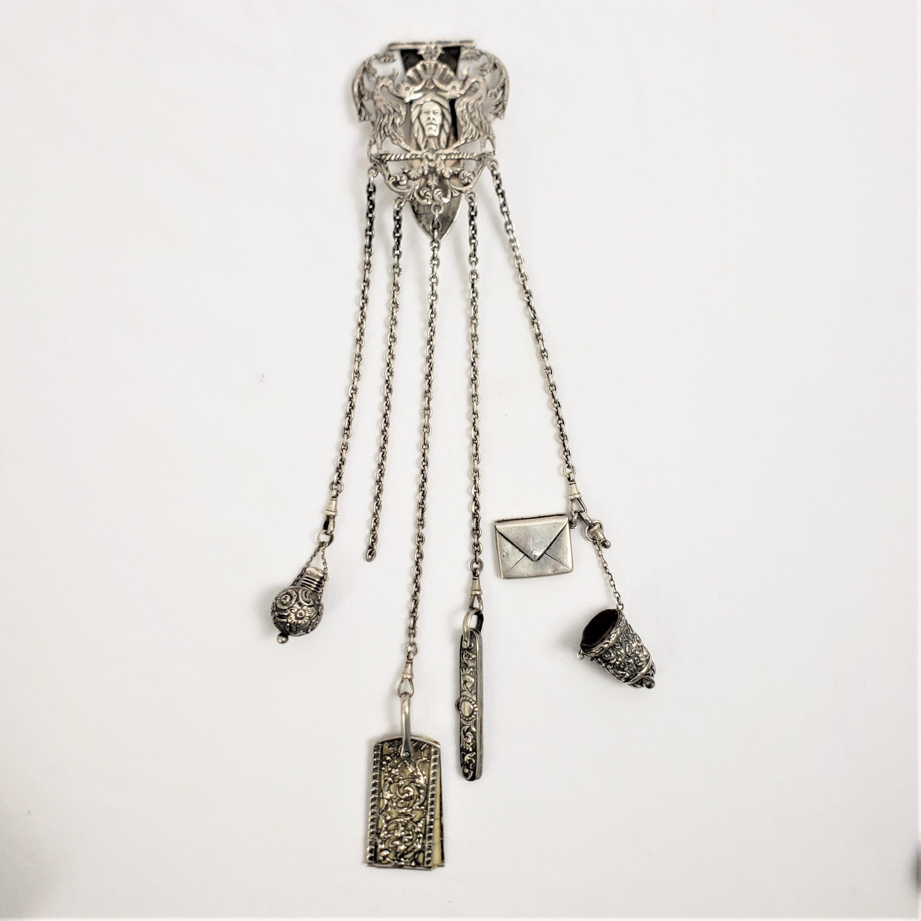 This chatelain originates from England and dates to approximately 1880 and done in the period Victorian style. This chatelaine is composed of sterling silver and features a clasp that is decorated with a stylized face with an extoc and grotesque