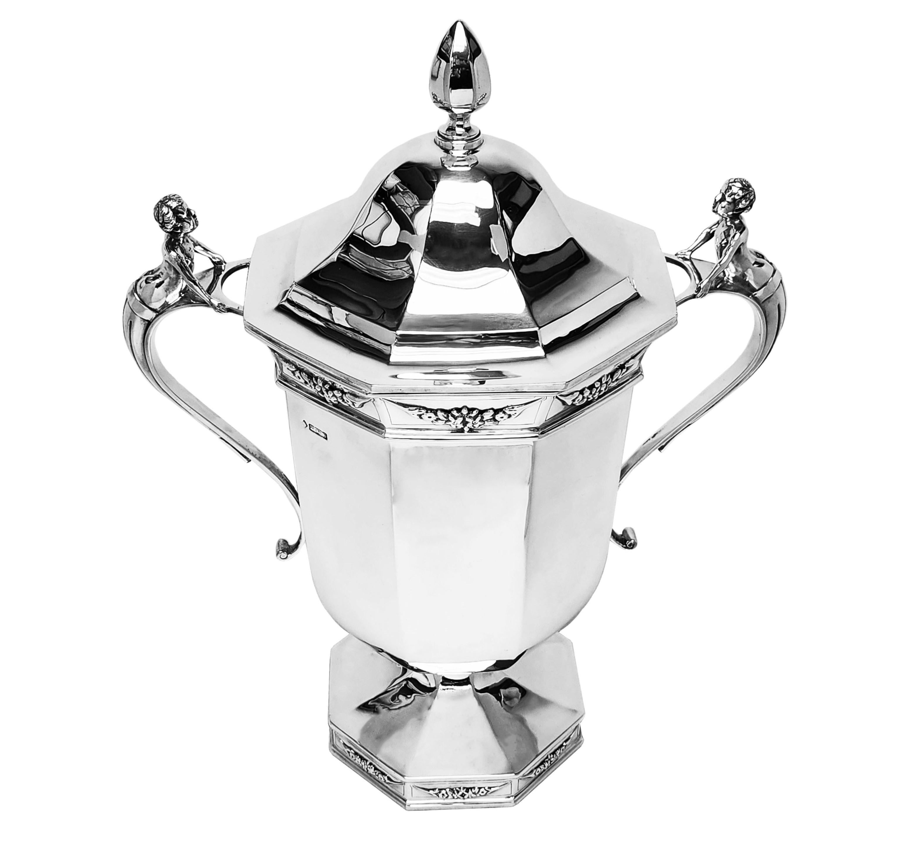 An impressive Antique Solid Silver Lidded Cup with an elegant octagonal shape. The Trophy has two impressive figural handles and has has an understated band of floral swags below the rim and on the foot. This Cup is suitable for use as a good size