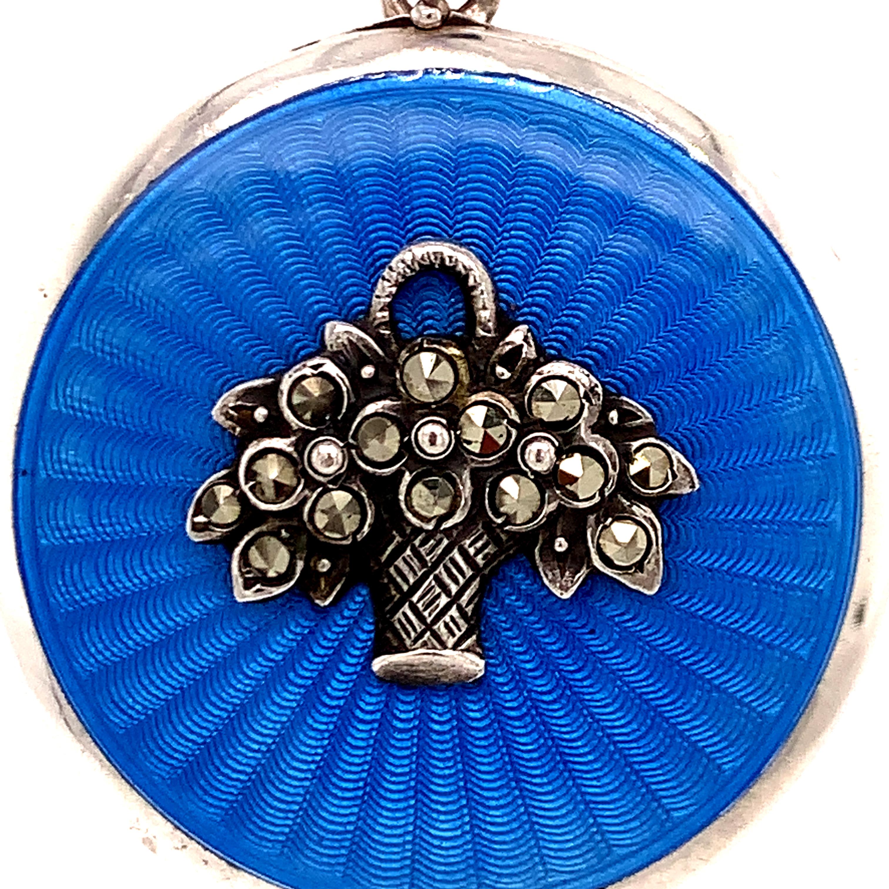 Beautiful locket:  round French blue guilloche enamel.  In the center is a graceful applied basket of flowers, accented with shimmering marcasites.  The locket opens to reveal spaces for two photographs, with original bezels.  Set in sterling