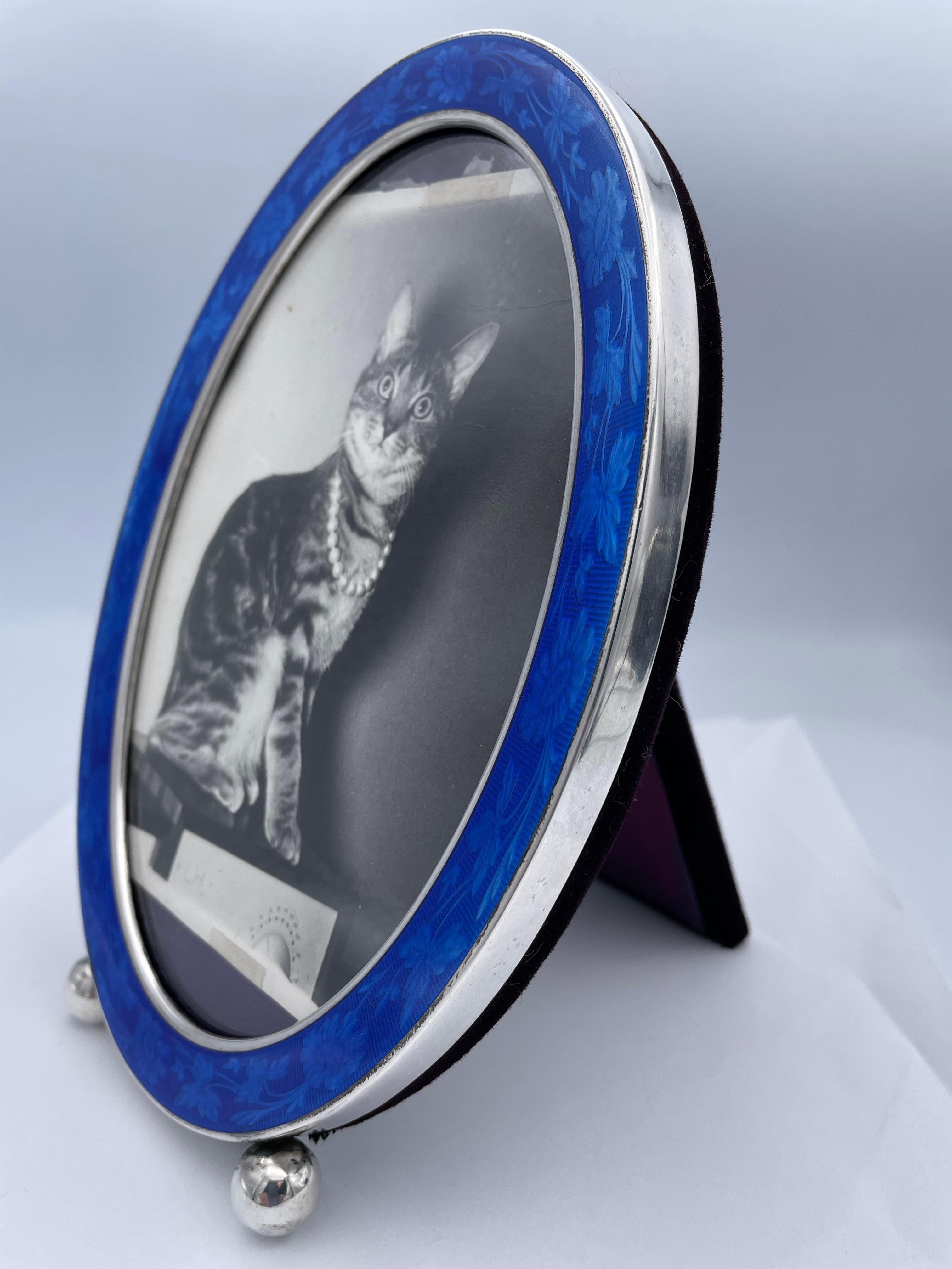 Beautiful antique picture frame:  a sterling silver oval, with a rich deep blue guilloche border. Embellished with an allover flower and leaf motif.  On two ball feet.  5 2/3