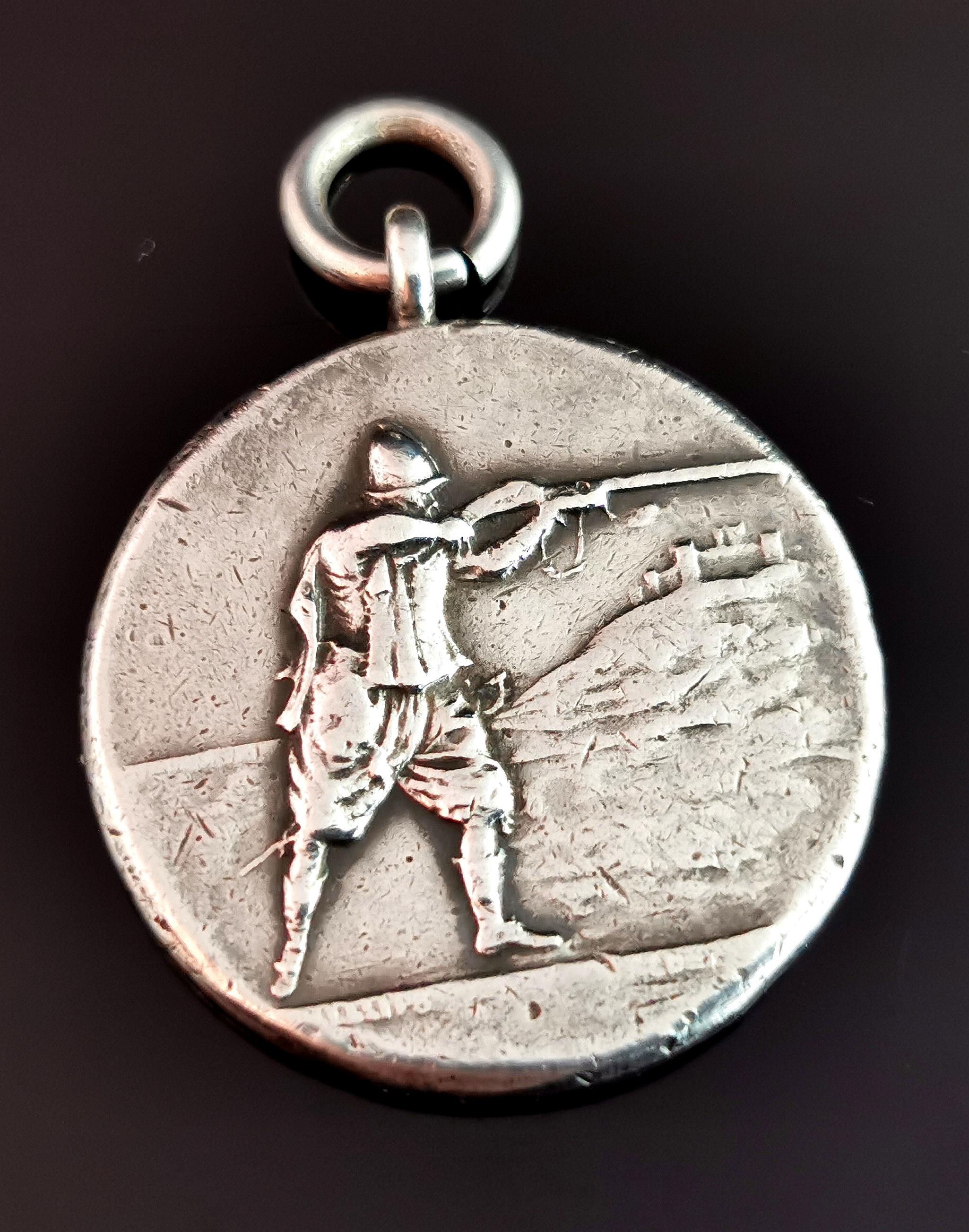 An attractive and unusual antique sterling silver fob pendant.

It is a harder to find fob with a unique design.

Circular shaped with a raised design and features a man with a rifle out shooting, presumably it was a hunting or shooting club