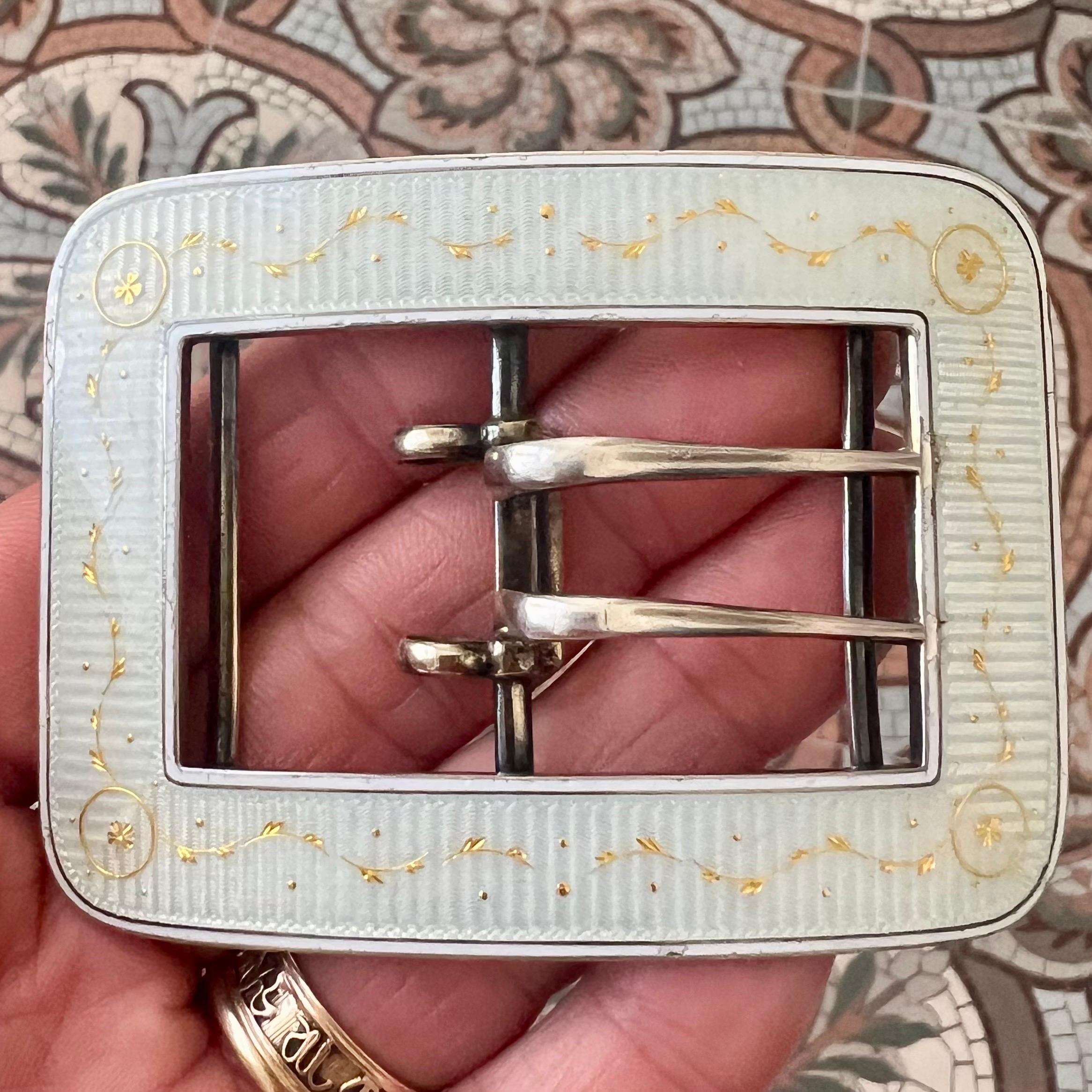 An elegant antique sterling silver buckle exquisitely decorated with white guilloché enamel and hand-painted gold details, dating to around 1900. This refined piece captures the sophistication of the Edwardian era, when delicate enamelwork and fine